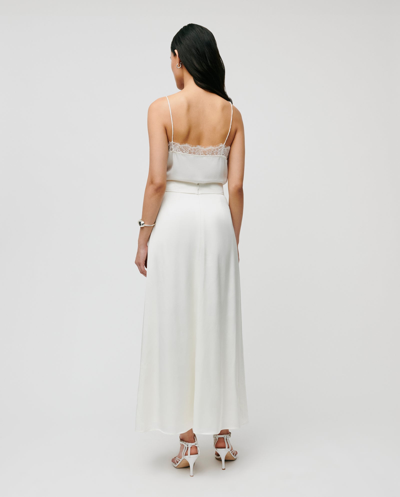 Woman seen from behind, wearing a white sleeveless ELAINA Top with lace trim and an IVY OAK SANNA Skirt, standing against a plain background.
