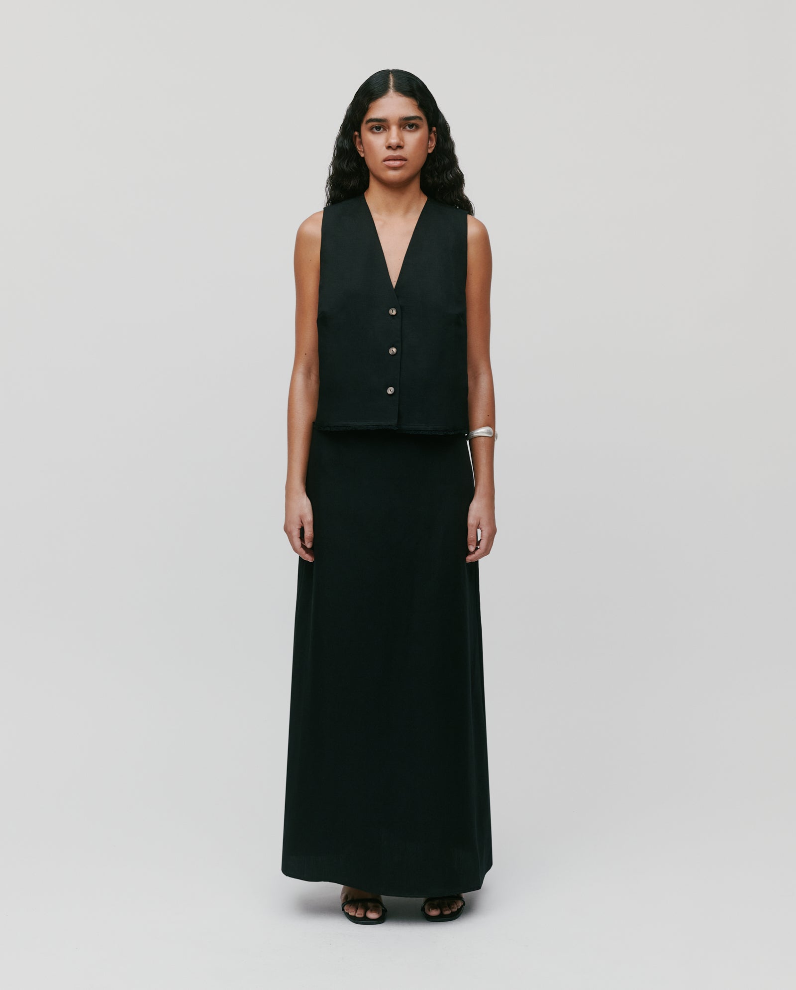 A woman models the IVY OAK SAMANTHA ANN Skirt, paired with a sleeveless black vest, standing against a plain light background.