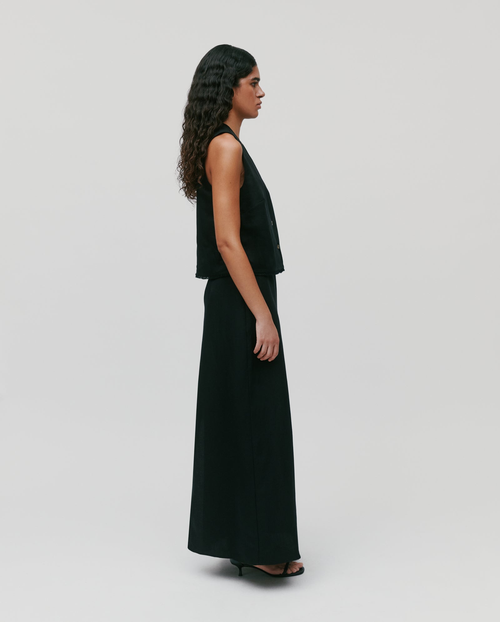 Woman with long curly hair wearing the SAMANTHA ANN Skirt by IVY OAK, styled with heels, standing in profile against a plain background.