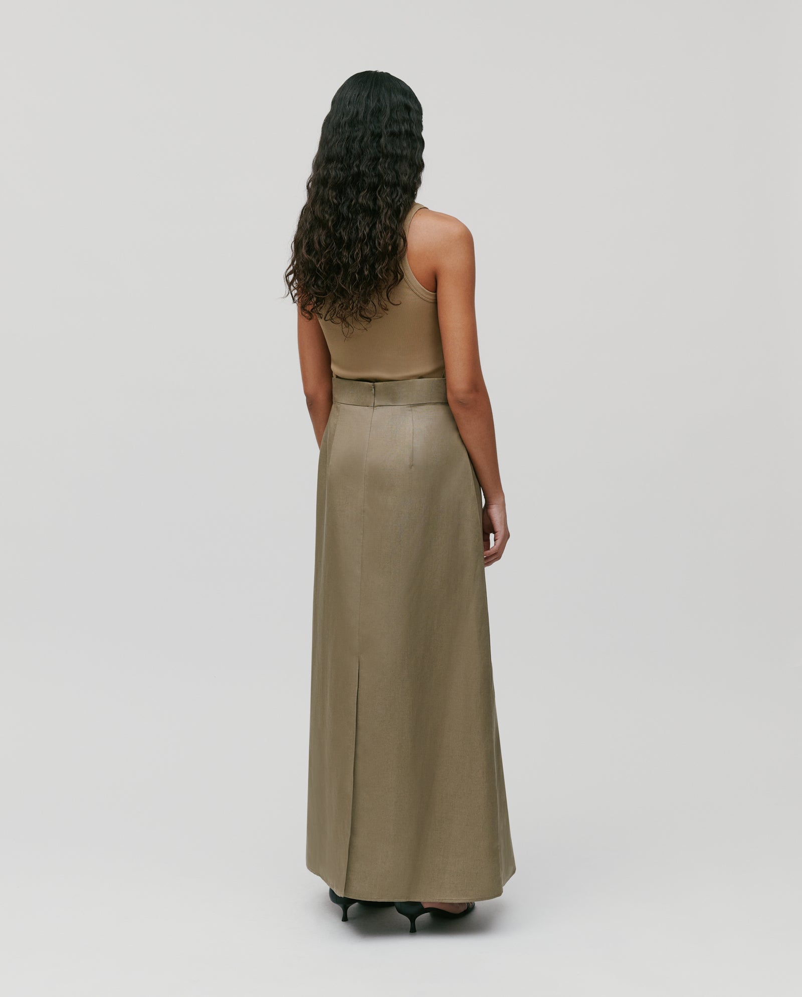 A woman with long curly hair wears a tan top and an IVY OAK SAMANTHA ANN Skirt, standing with her back to the camera.