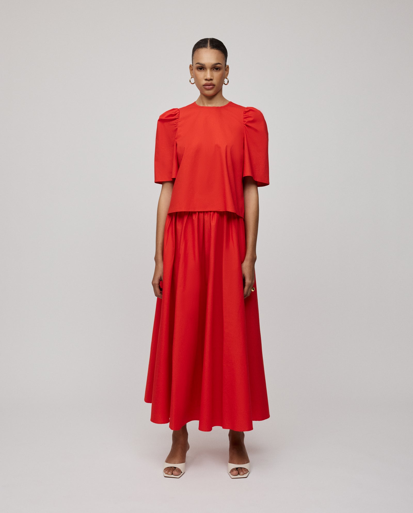A woman in a bright red puff-sleeve top and the IVY OAK SIENNA Skirt—a voluminous, long cotton skirt with a defined waistband—stands against a plain background.