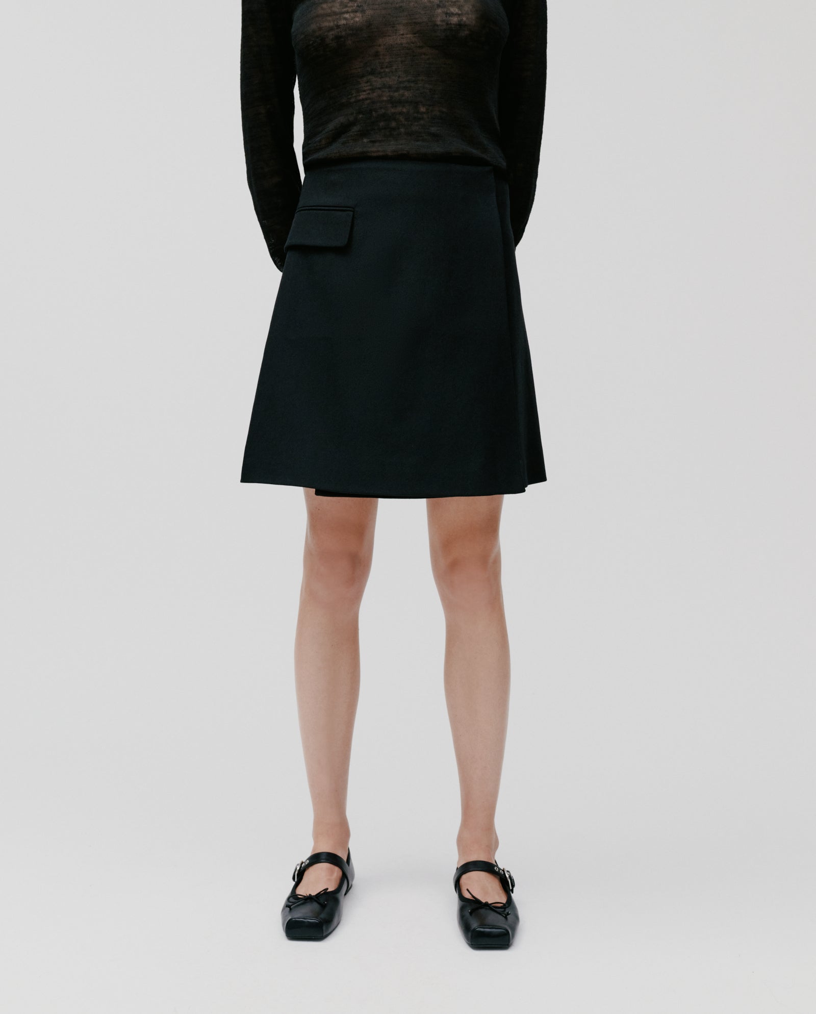 A person wearing a sheer black top, the IVY OAK STEVIE Skirt, and black shoes stands against a plain background.