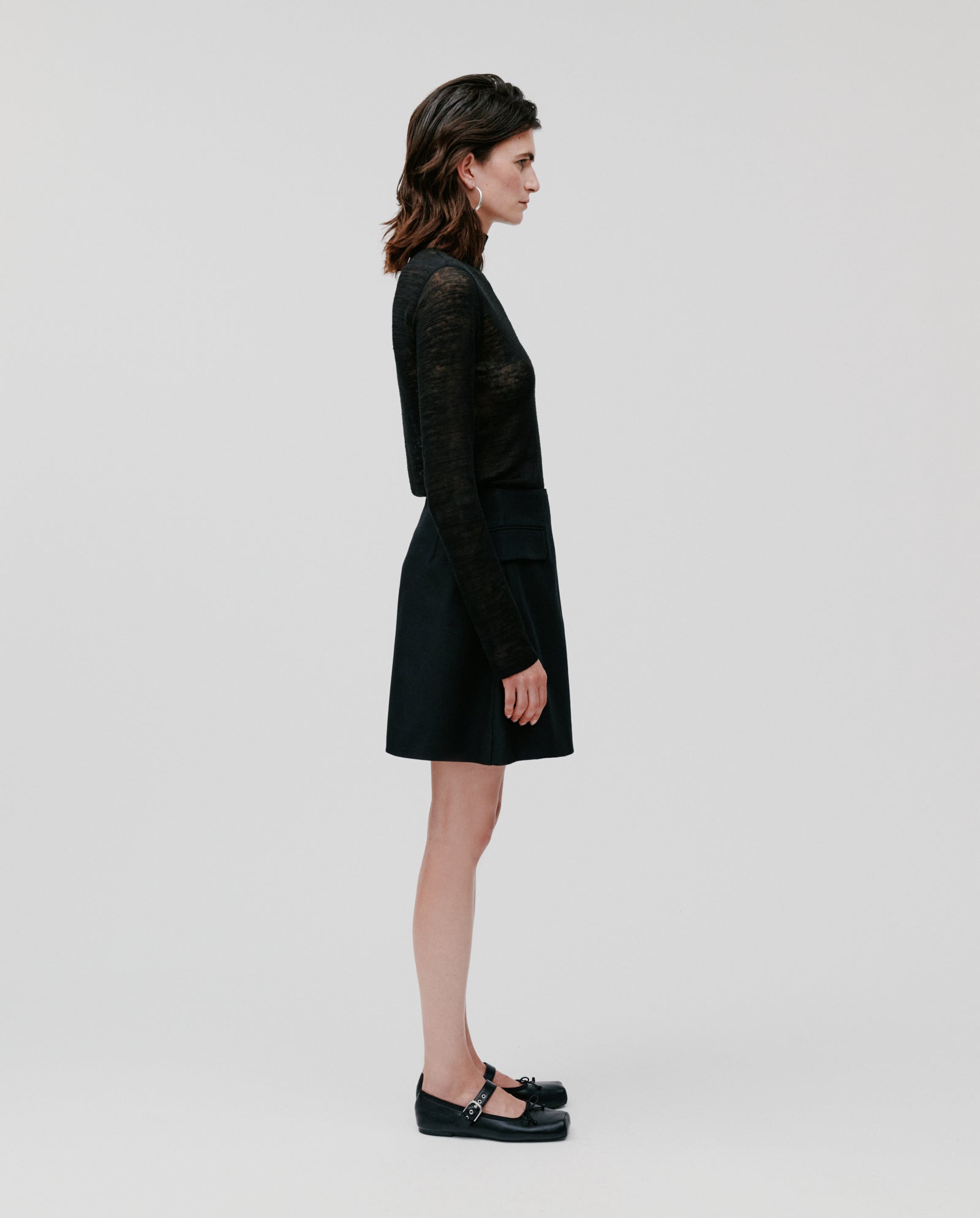 A woman in profile models the IVY OAK STEVIE Skirt and a black long-sleeve top against a plain white background.
