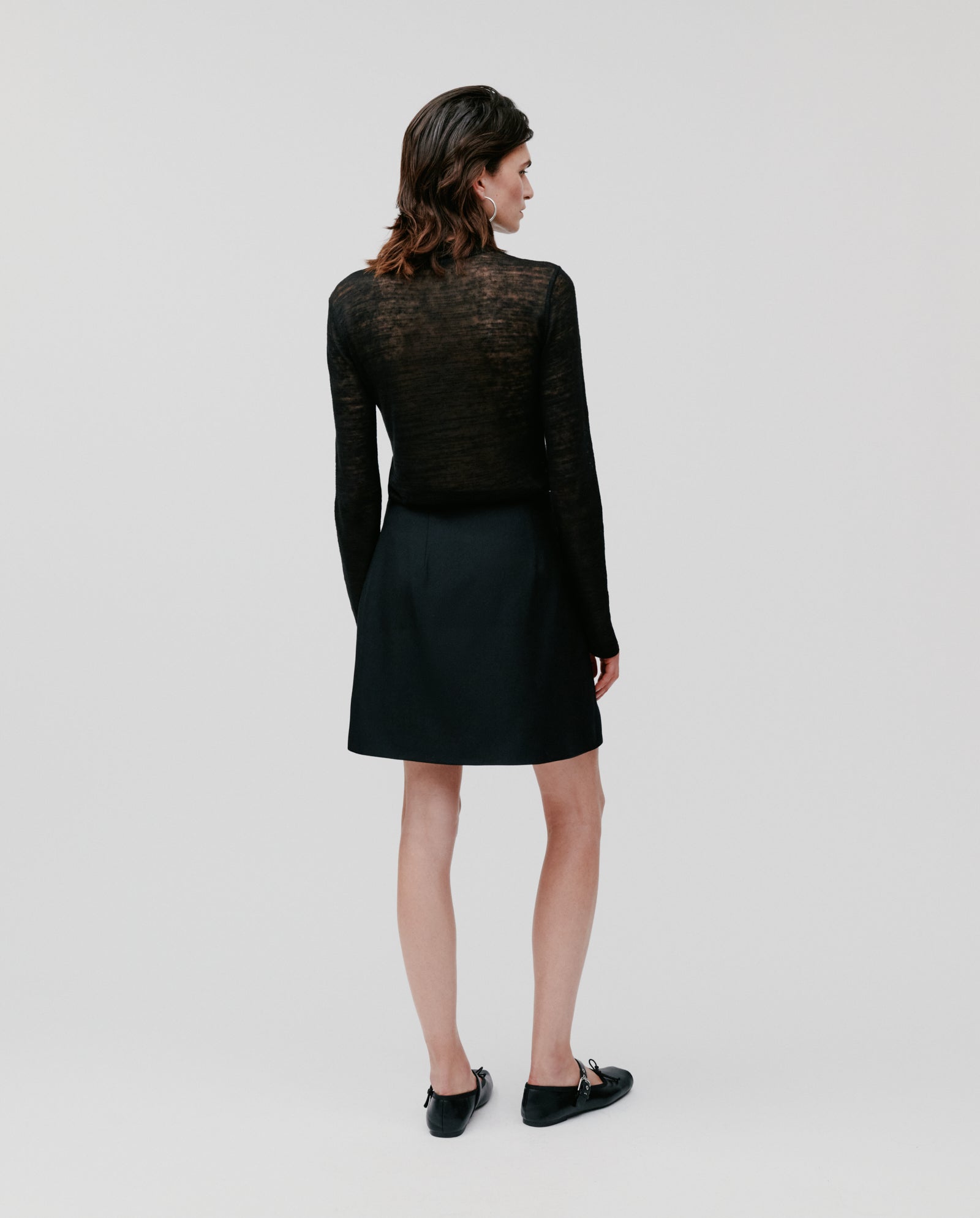 A person stands against a plain background wearing the IVY OAK STEVIE Skirt paired with a black long-sleeve top and black shoes.