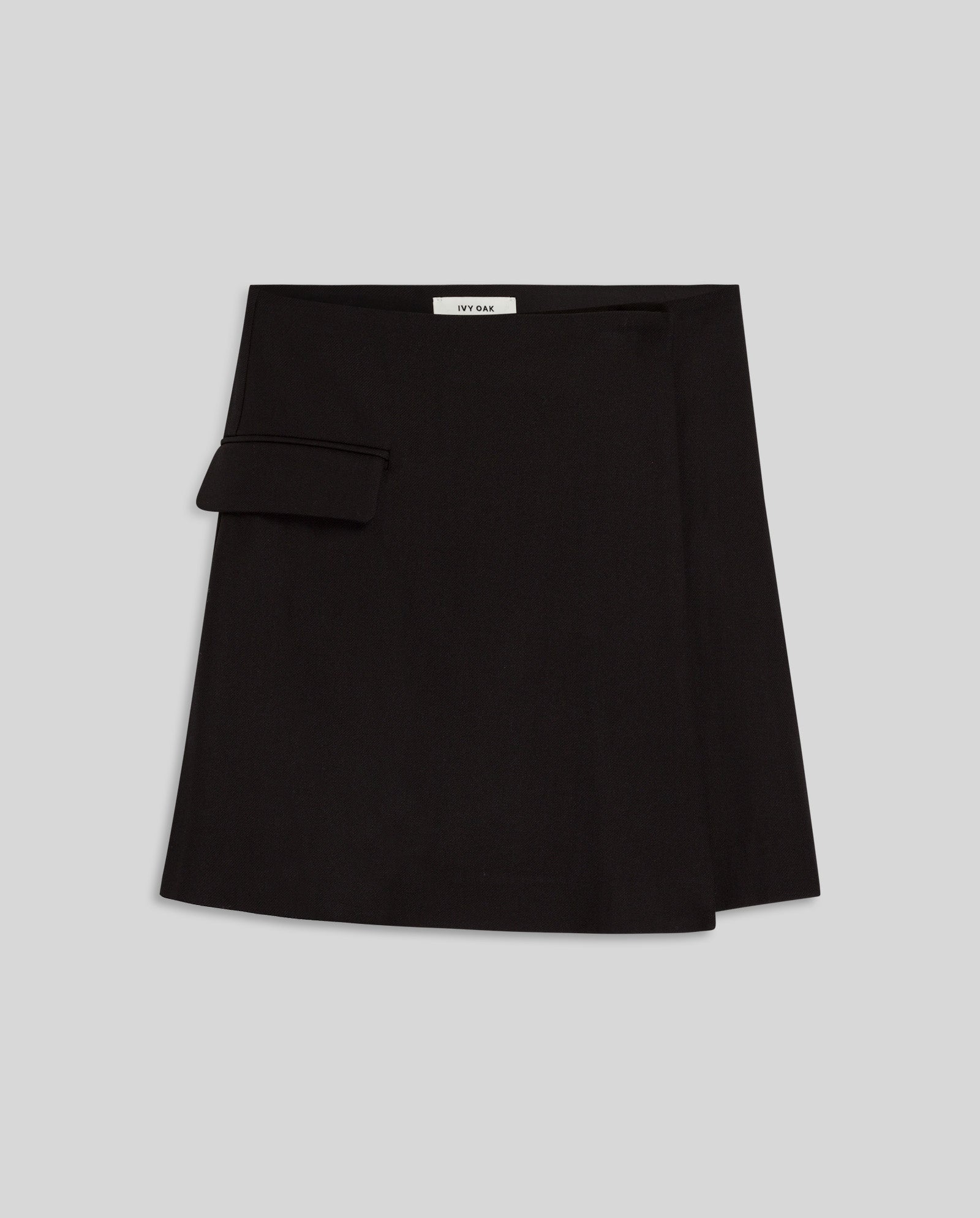 The IVY OAK STEVIE Skirt is a black wrap mini skirt with a small side pocket, shown on a plain light gray background. This stylish skirt combines chic design with everyday convenience.