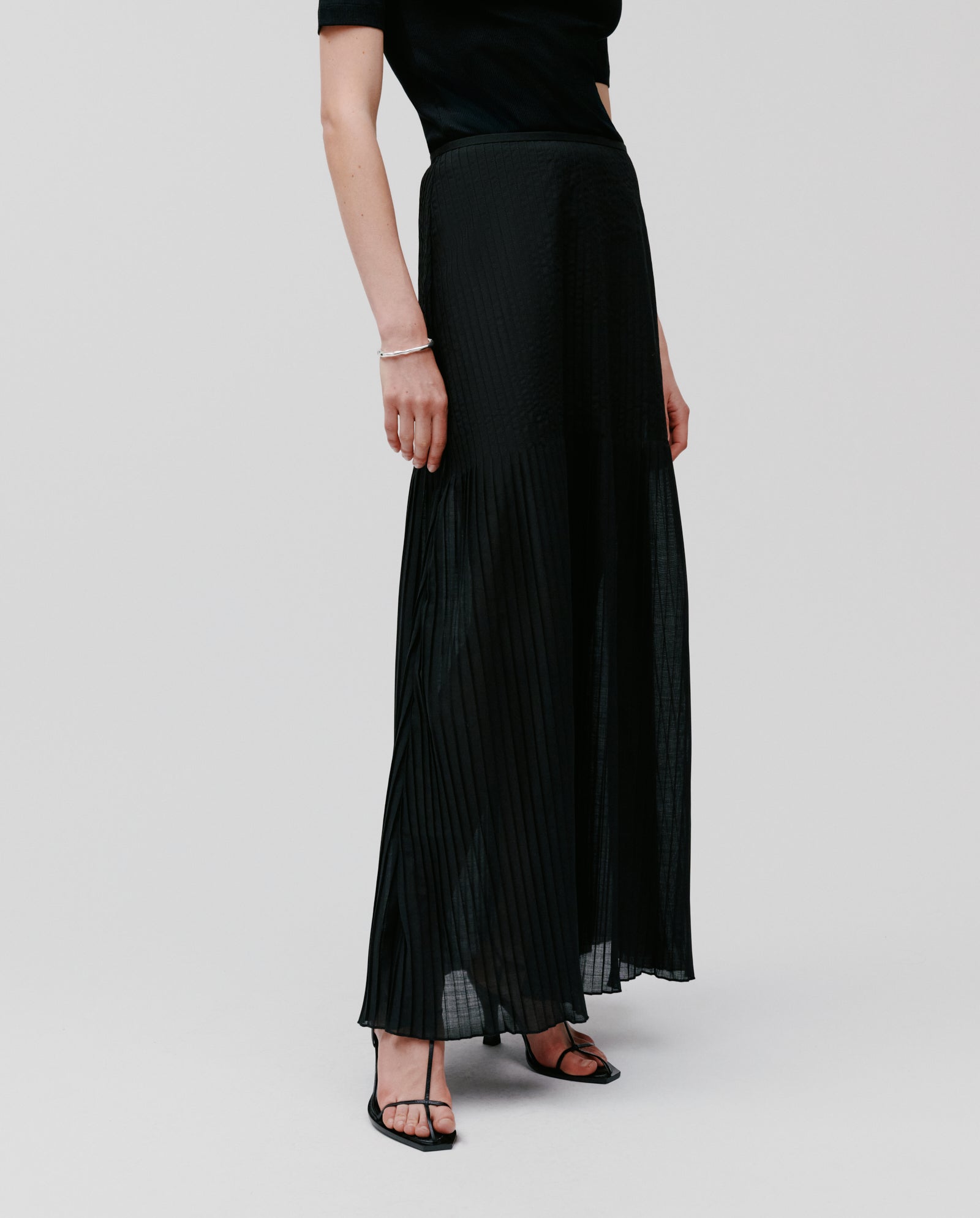 A person models the IVY OAK SALENA Skirt in black, styled with a matching top and heeled sandals, standing against a plain background.