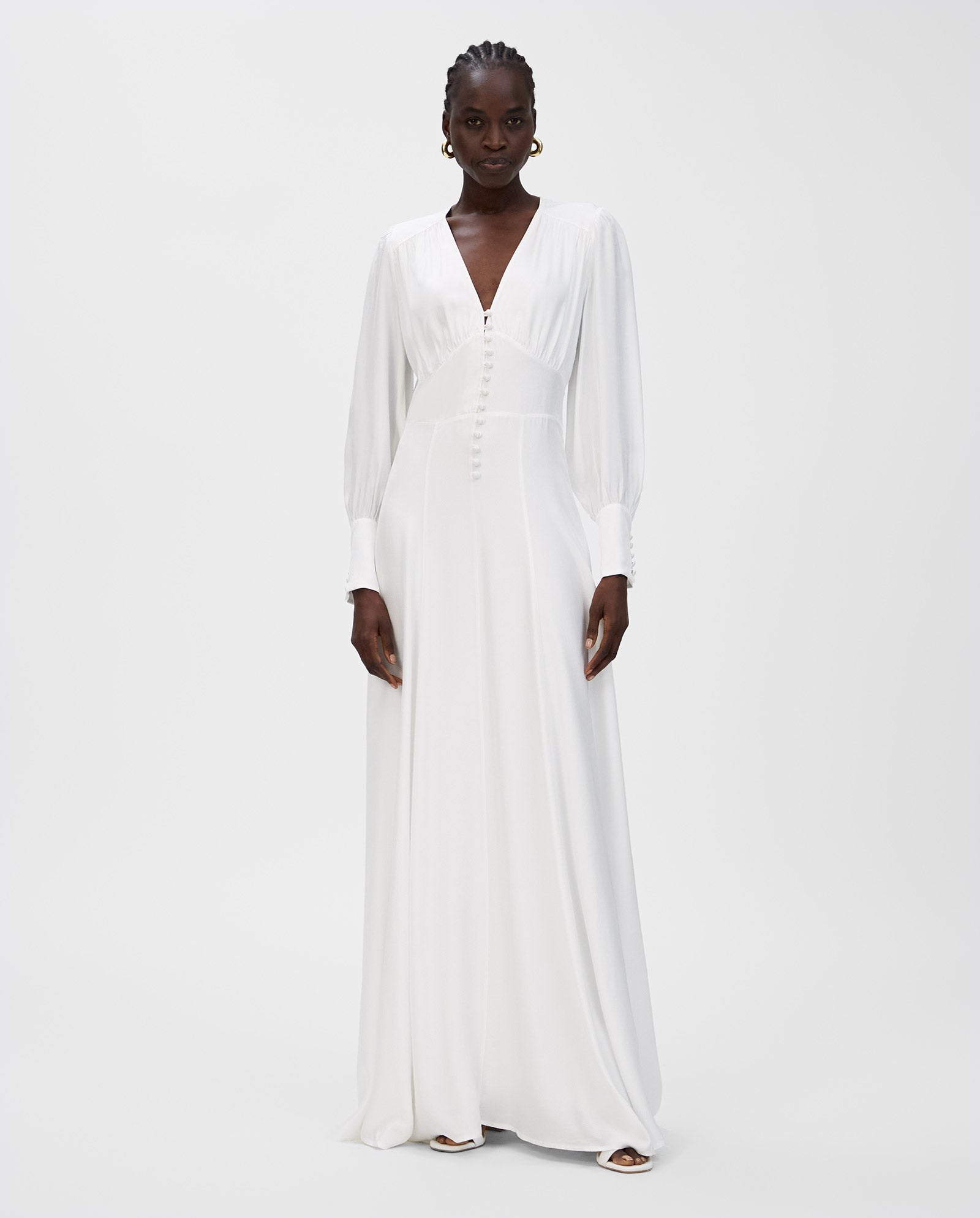A woman in the IVY OAK NYSSA ROSE Bridaldress—featuring a deep V-neckline, maxi length, and voluminous sleeves—stands against a plain background.