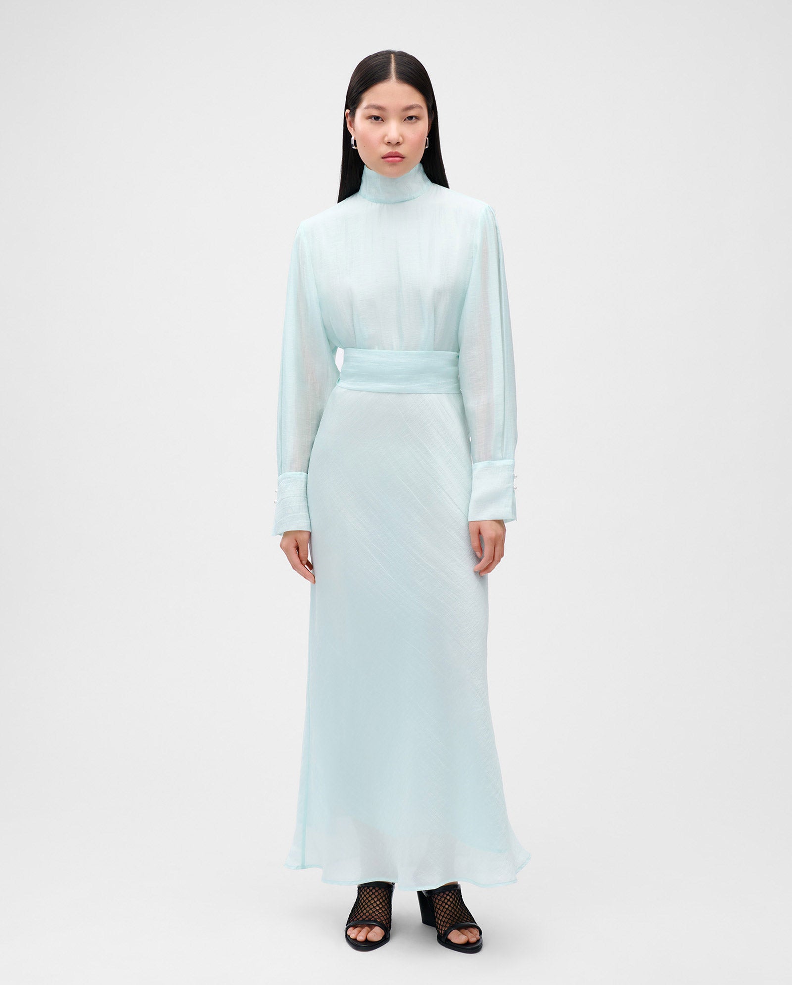 A woman in a light blue IVY OAK MALINA Dress with organza fabric, midi length, flared skirt, and black heeled sandals stands against a plain background.