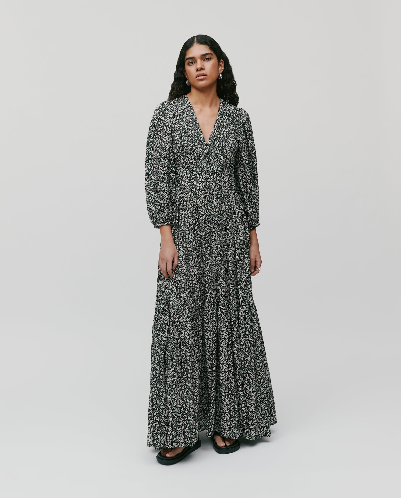 Woman wearing the IVY OAK DREA Dress, a long black floral dress with V-neck and long sleeves, standing against a plain light background.
