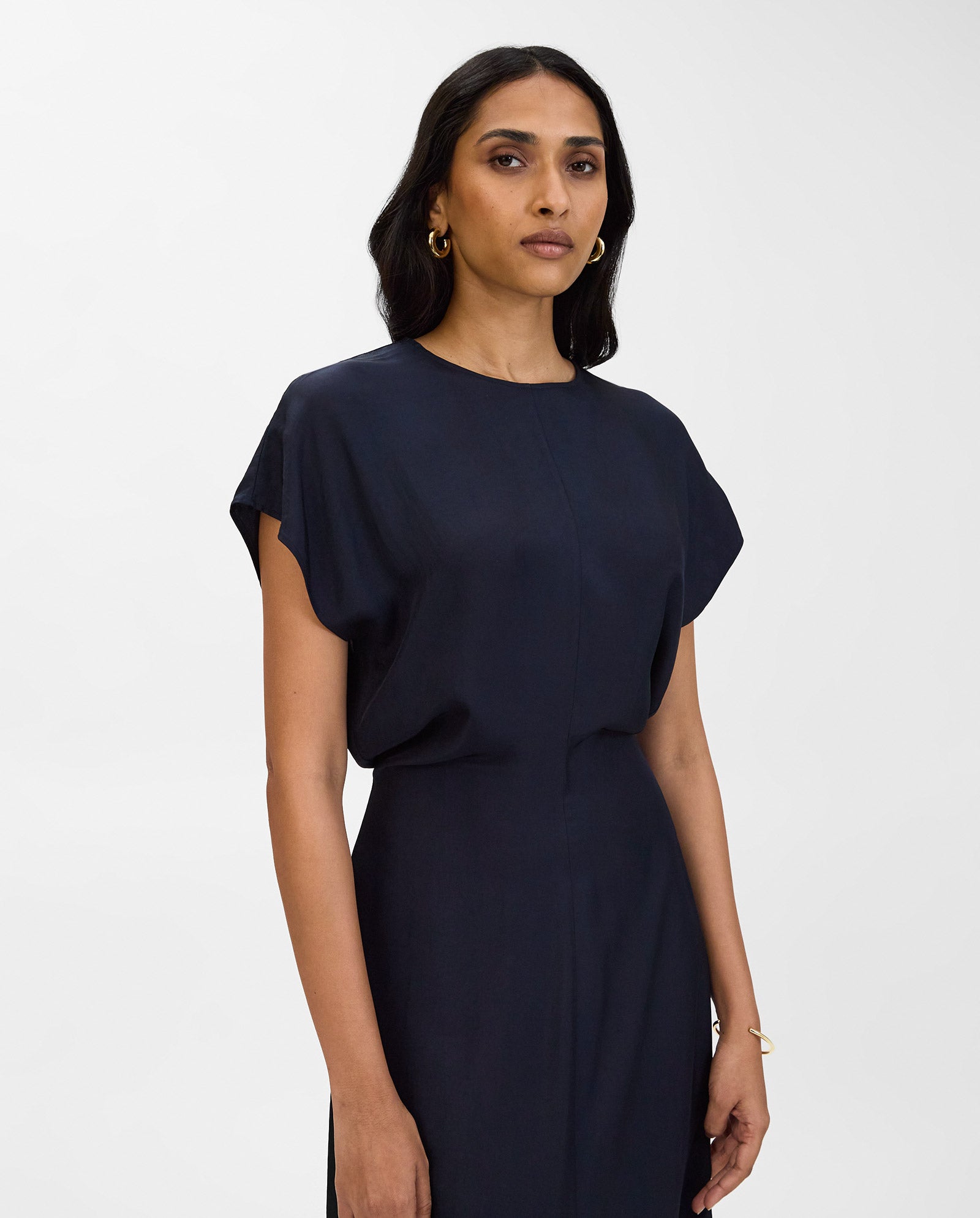 A woman wears the IVY OAK MARLIS SUE Dress in navy, featuring a fitted waist, standing against a white background and looking confidently at the camera.
