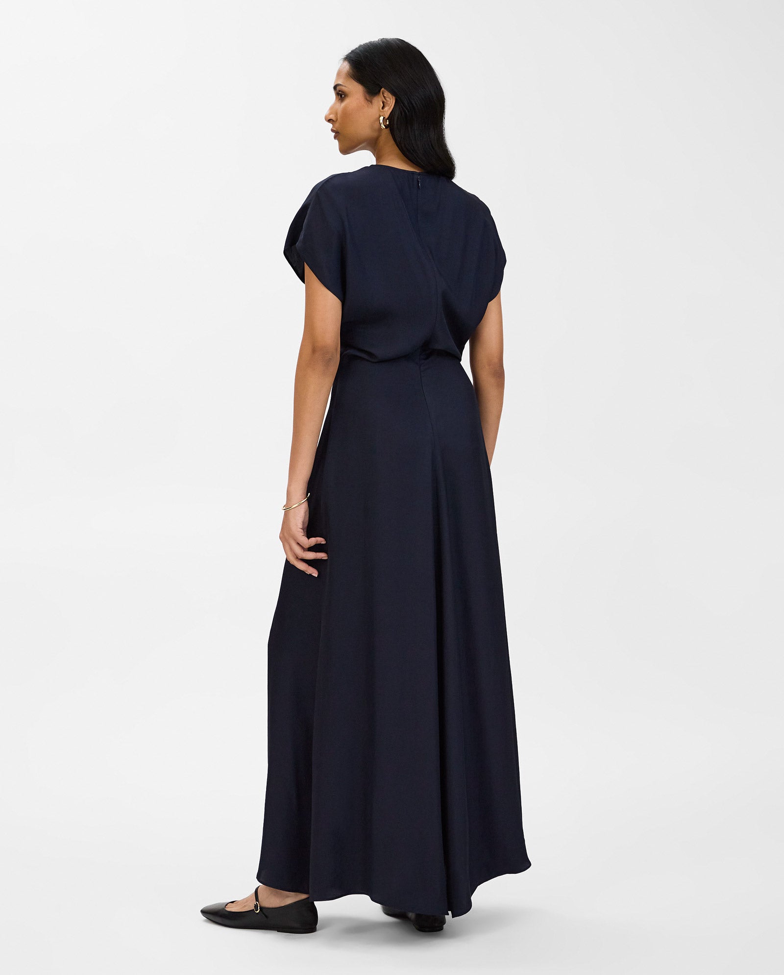 Woman in an IVY OAK MARLIS SUE navy blue short-sleeve maxi dress with a fitted waist and black flats, standing and facing away.
