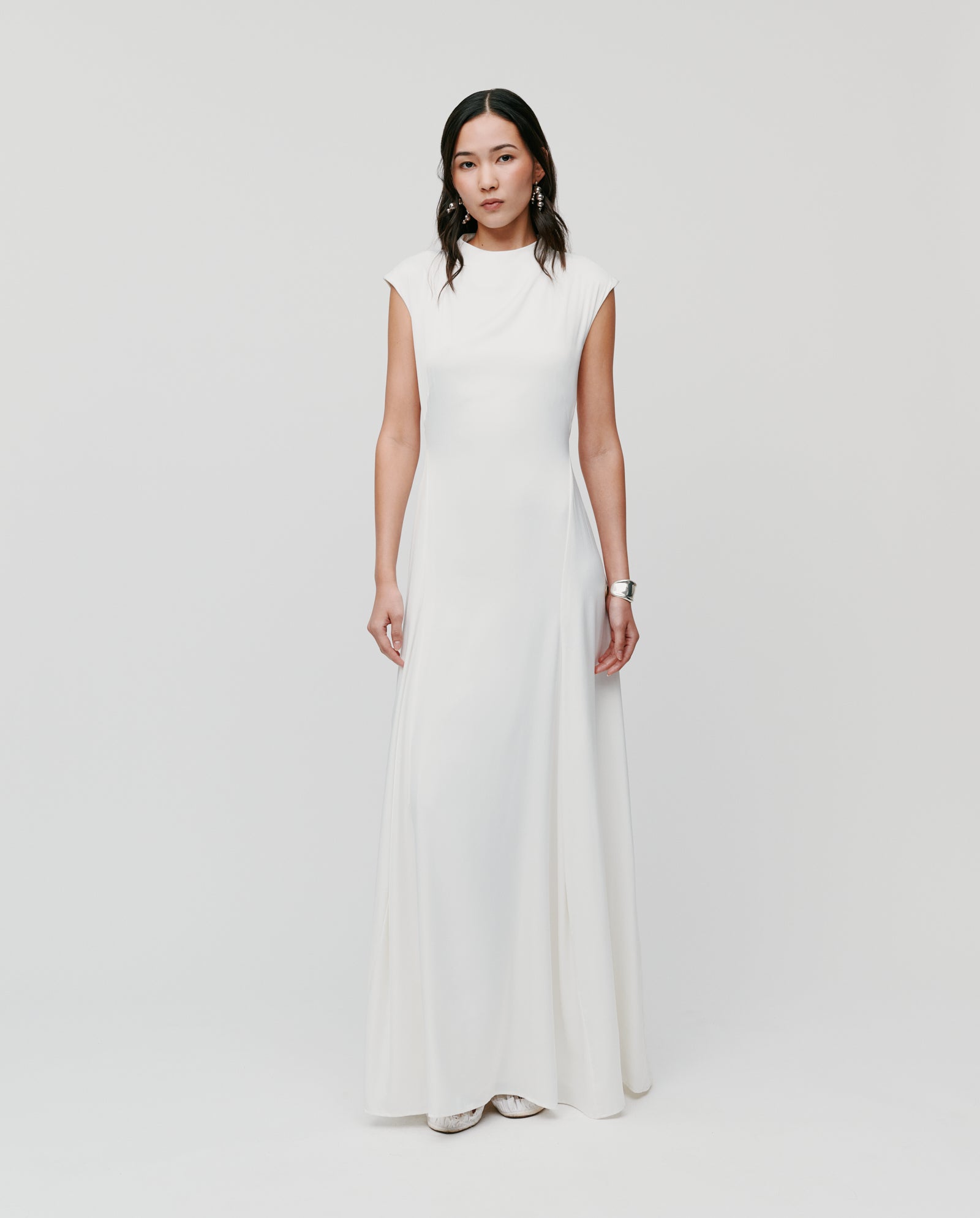 Woman in a simple, sleeveless IVY OAK MARCELLA LIZ Dress with subtle godets in the skirt, standing against a plain white background.