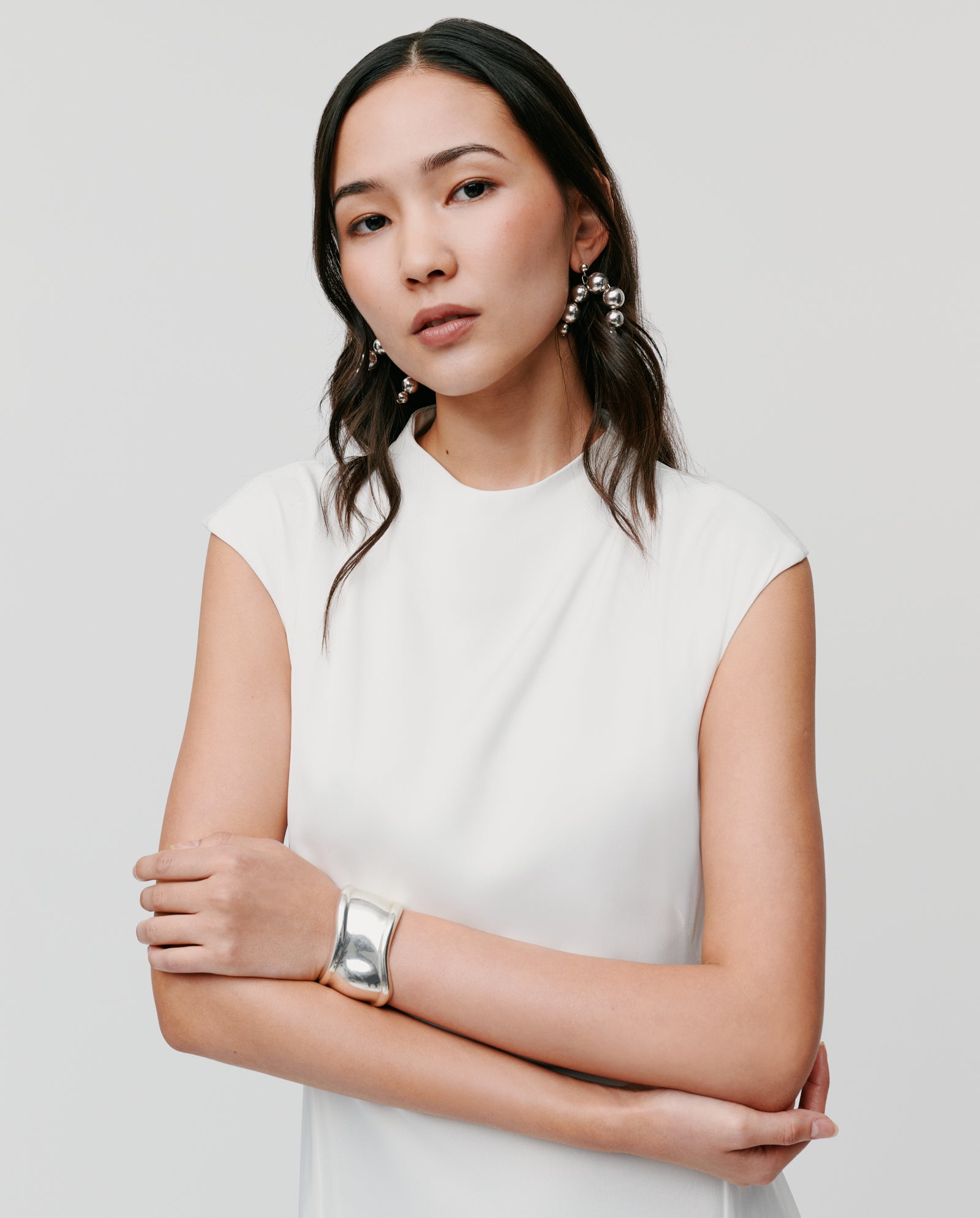 Woman in an IVY OAK MARCELLA LIZ Dress with wavy hair, silver jewelry, and a stand-up collar poses with arms crossed against a plain background.