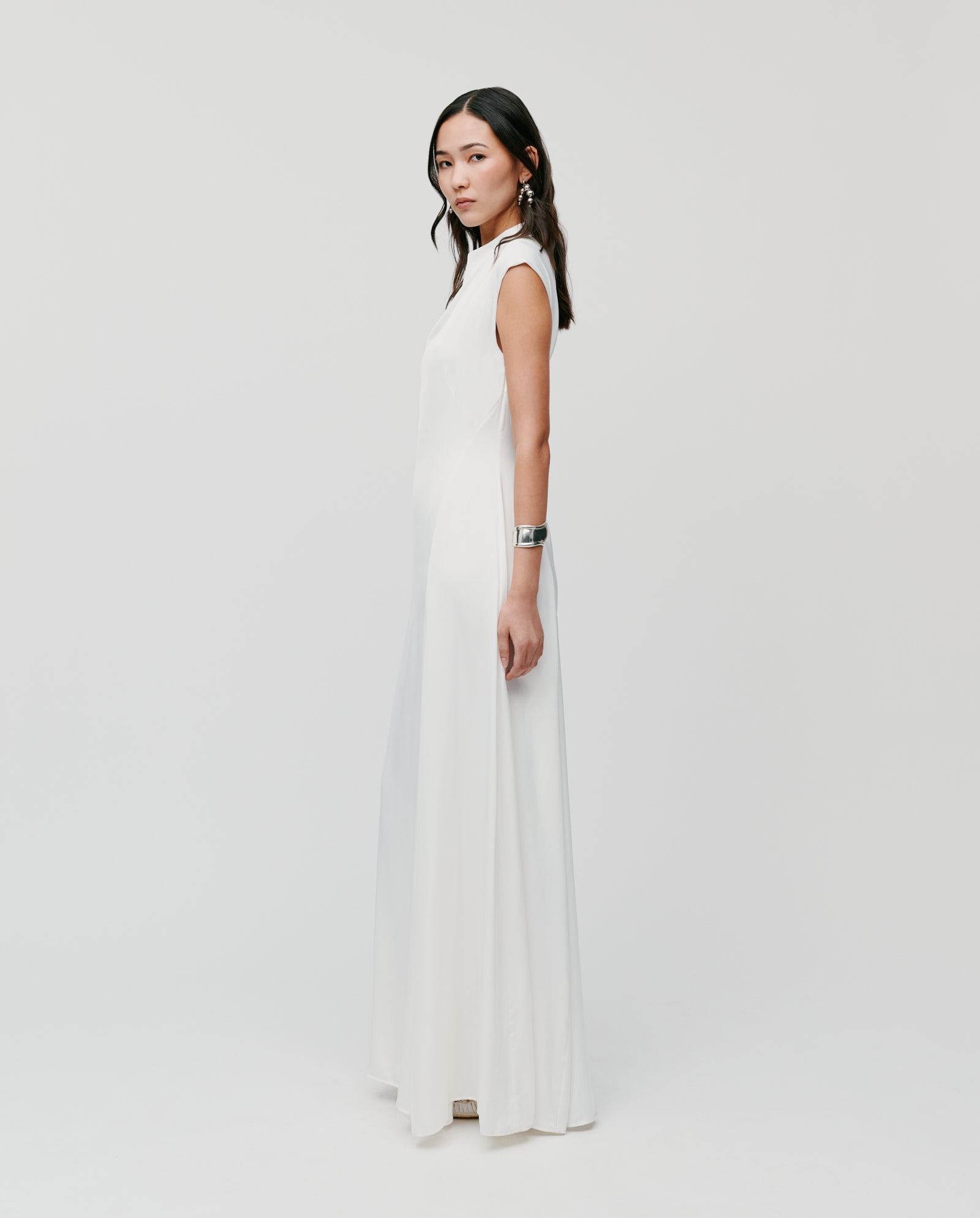 Woman in a sleeveless IVY OAK MARCELLA LIZ Dress with a flared skirt, standing sideways against a plain white background.
