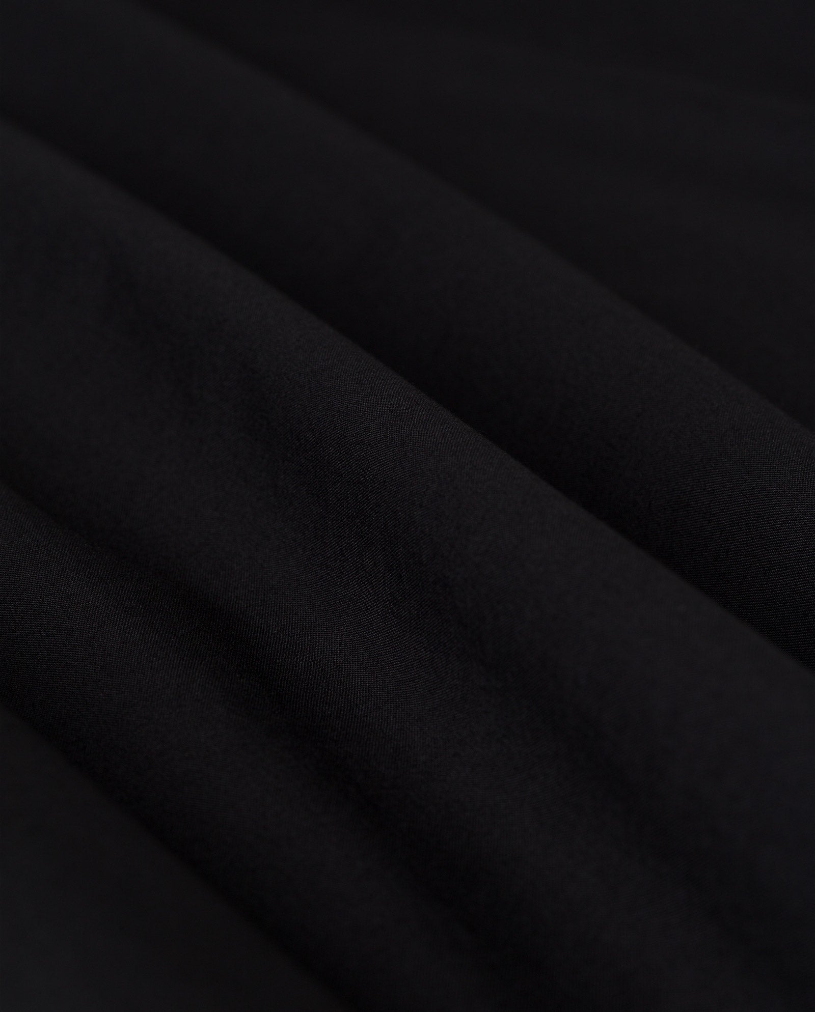 Close-up of black fabric with soft, diagonal folds and a smooth texture, echoing the refined pintucks found in the MARYTHA Dress by IVY OAK.