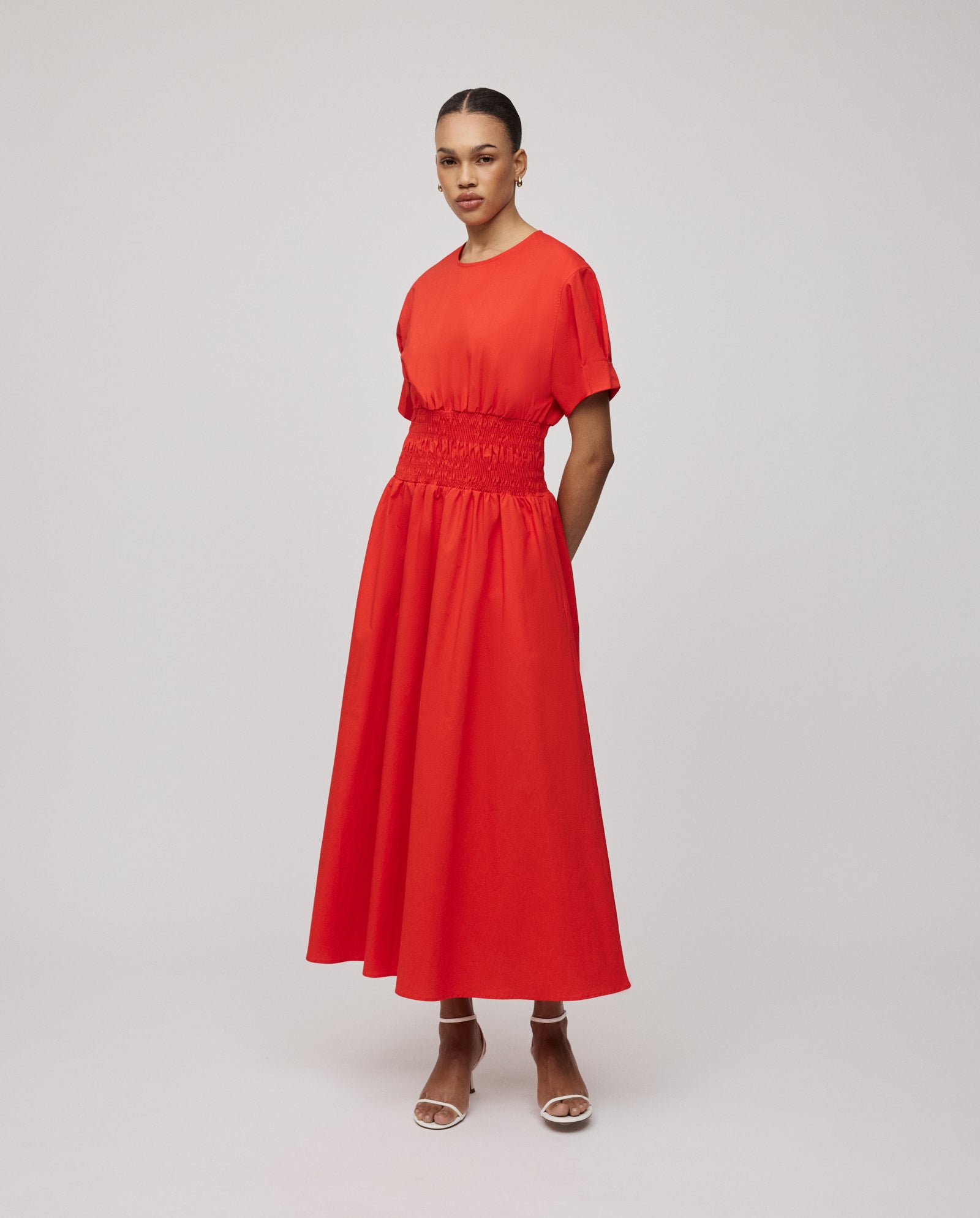 A woman wearing a bright red, V-neck MARYTHA dress by IVY OAK with short sleeves and maxi length, paired with white sandals, stands against a plain background.