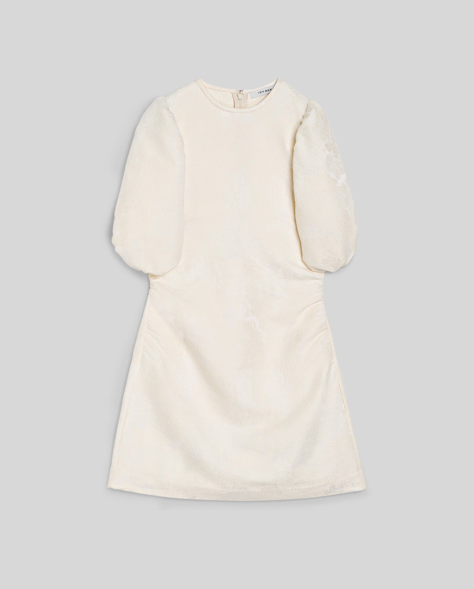 The IVY OAK NISSA Dress is an ivory jacquard mini dress with short puff sleeves, a fitted waist, round neckline, and a back zipper, shown laid flat on a gray background.