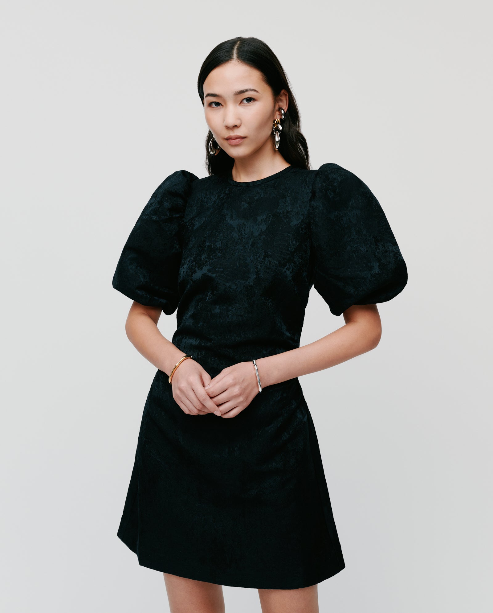A woman wearing an IVY OAK NISSA Dress with puff sleeves stands against a plain light background, hands clasped.