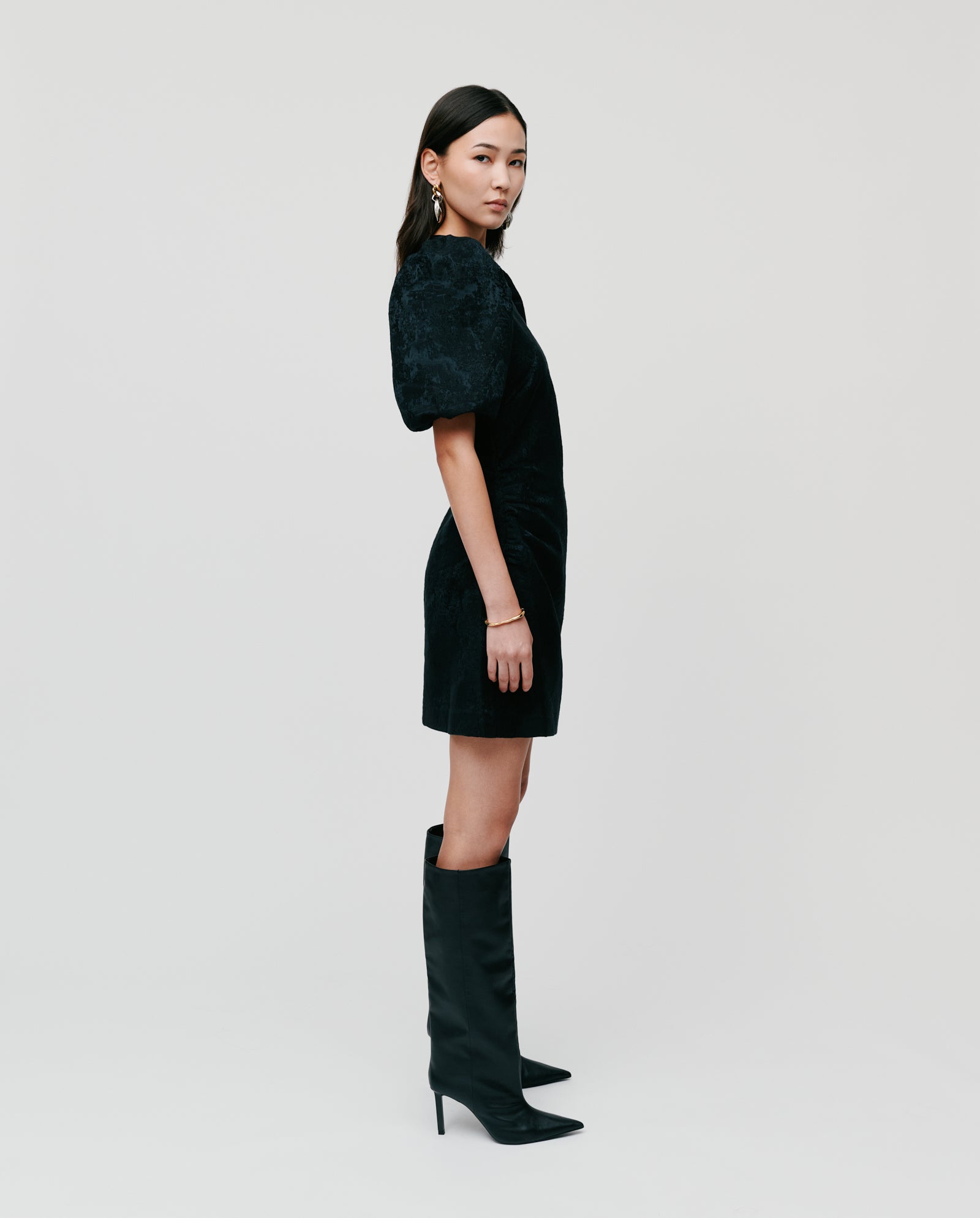 Woman in an IVY OAK NISSA Dress with jacquard fabric and puff sleeves, paired with knee-high boots, stands sideways against a plain white background.