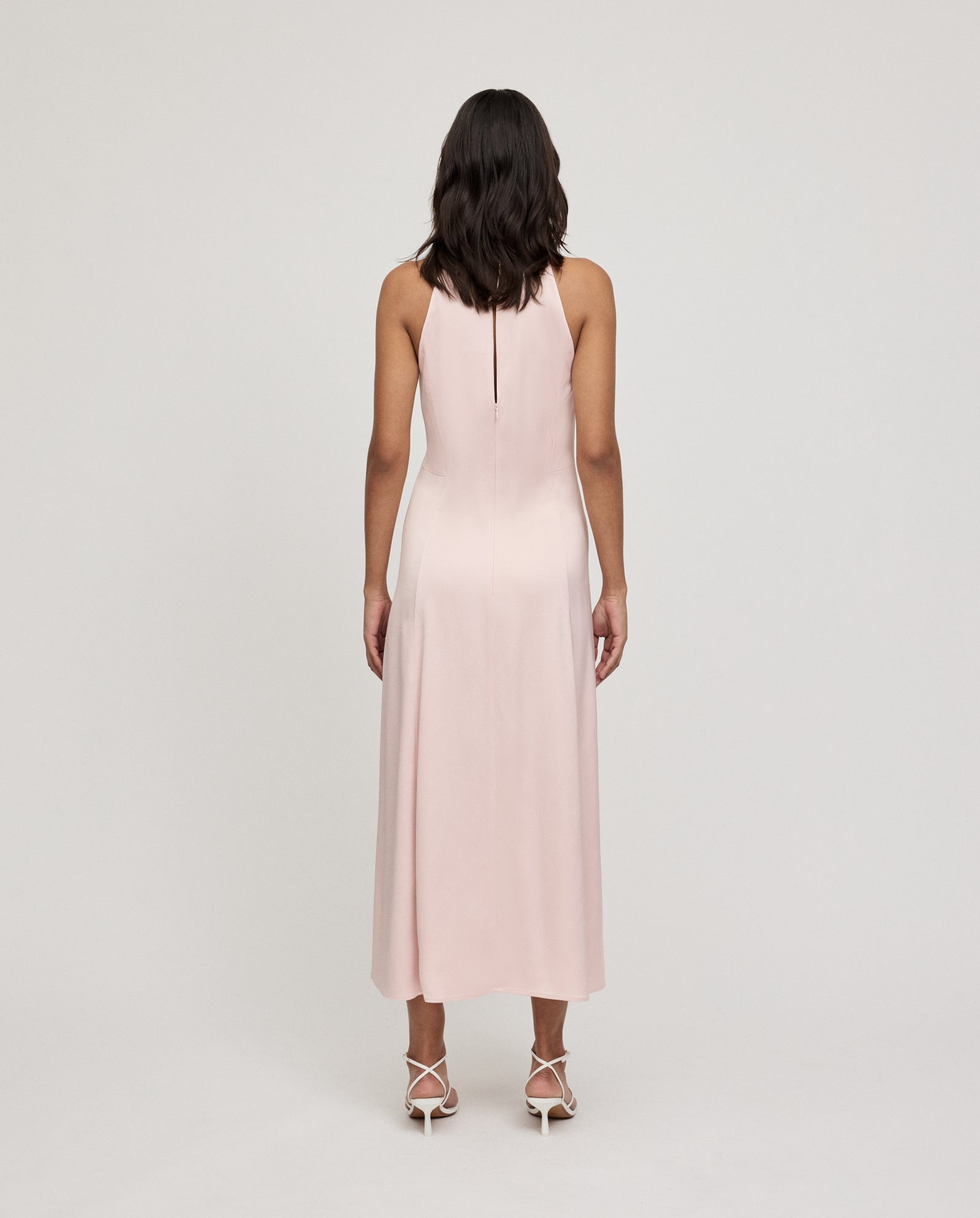 Woman wearing the IVY OAK DARCI ANN sleeveless light pink American shoulder midi dress with heels, standing facing away from the camera.