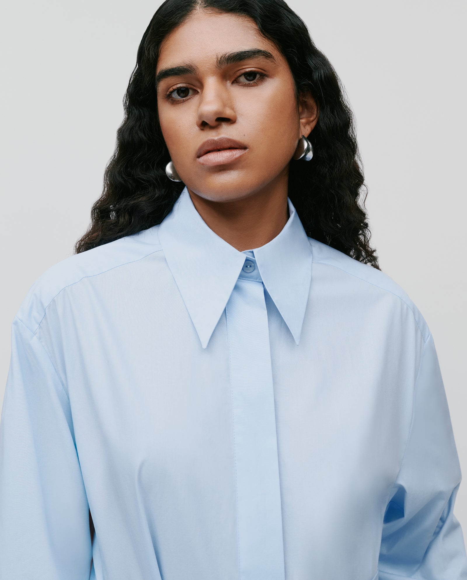 Woman with long curly hair wears the IVY OAK DINA ROSA Dress and silver hoop earrings, looking at the camera.