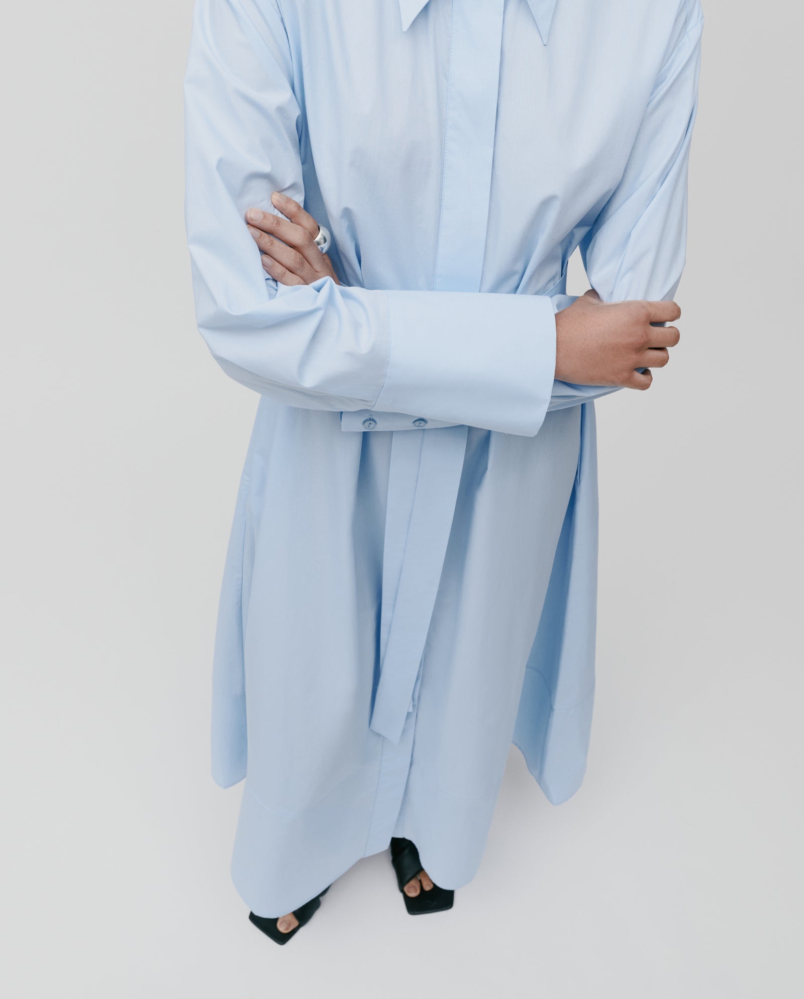 Person in a light blue DINA ROSA Dress by IVY OAK with adjustable cuffs, crossing their arms and wearing black open-toe shoes, seen from above.