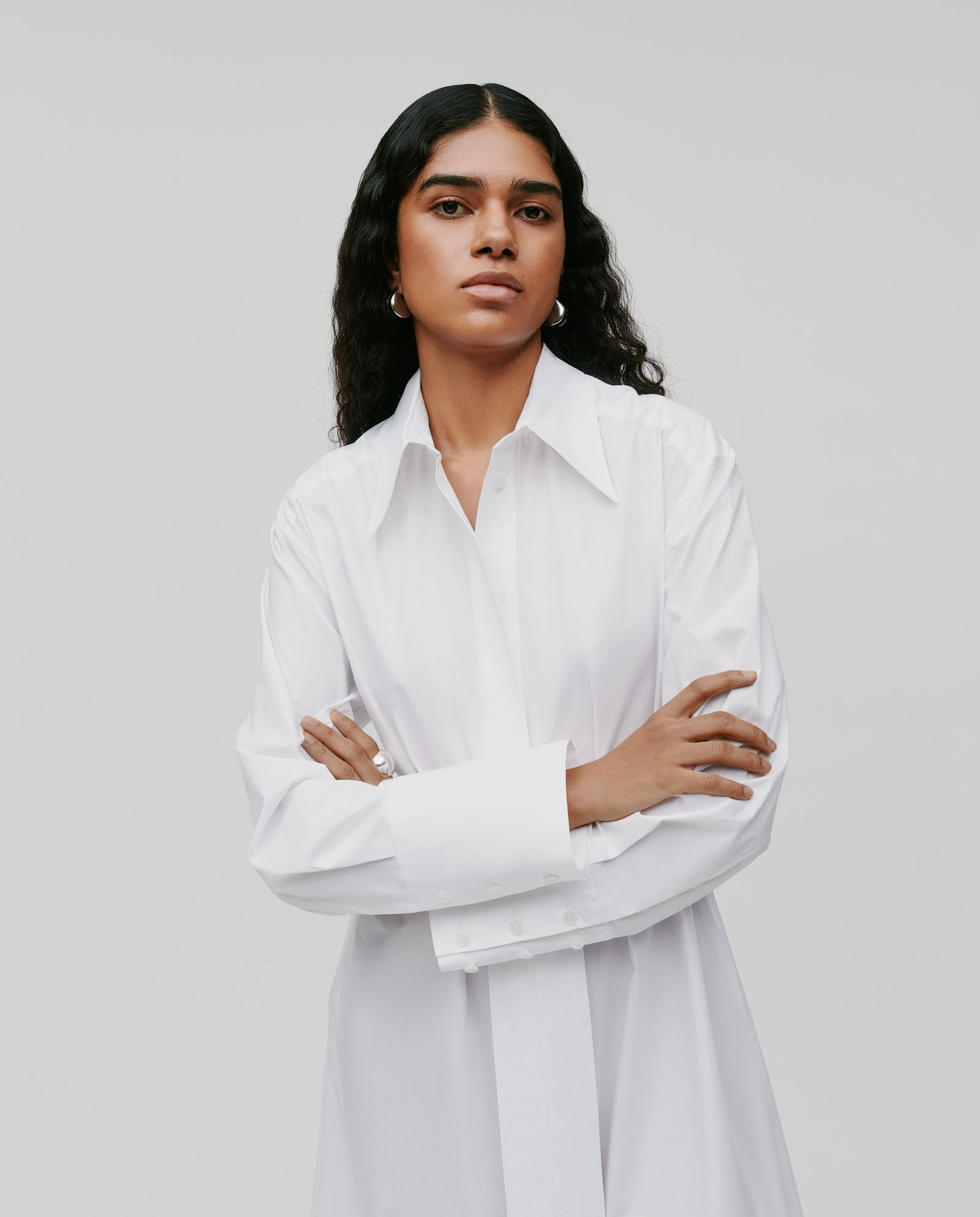 A person with long dark hair wears the IVY OAK DINA ROSA Dress, featuring adjustable cuffs, standing with arms crossed against a plain background.
