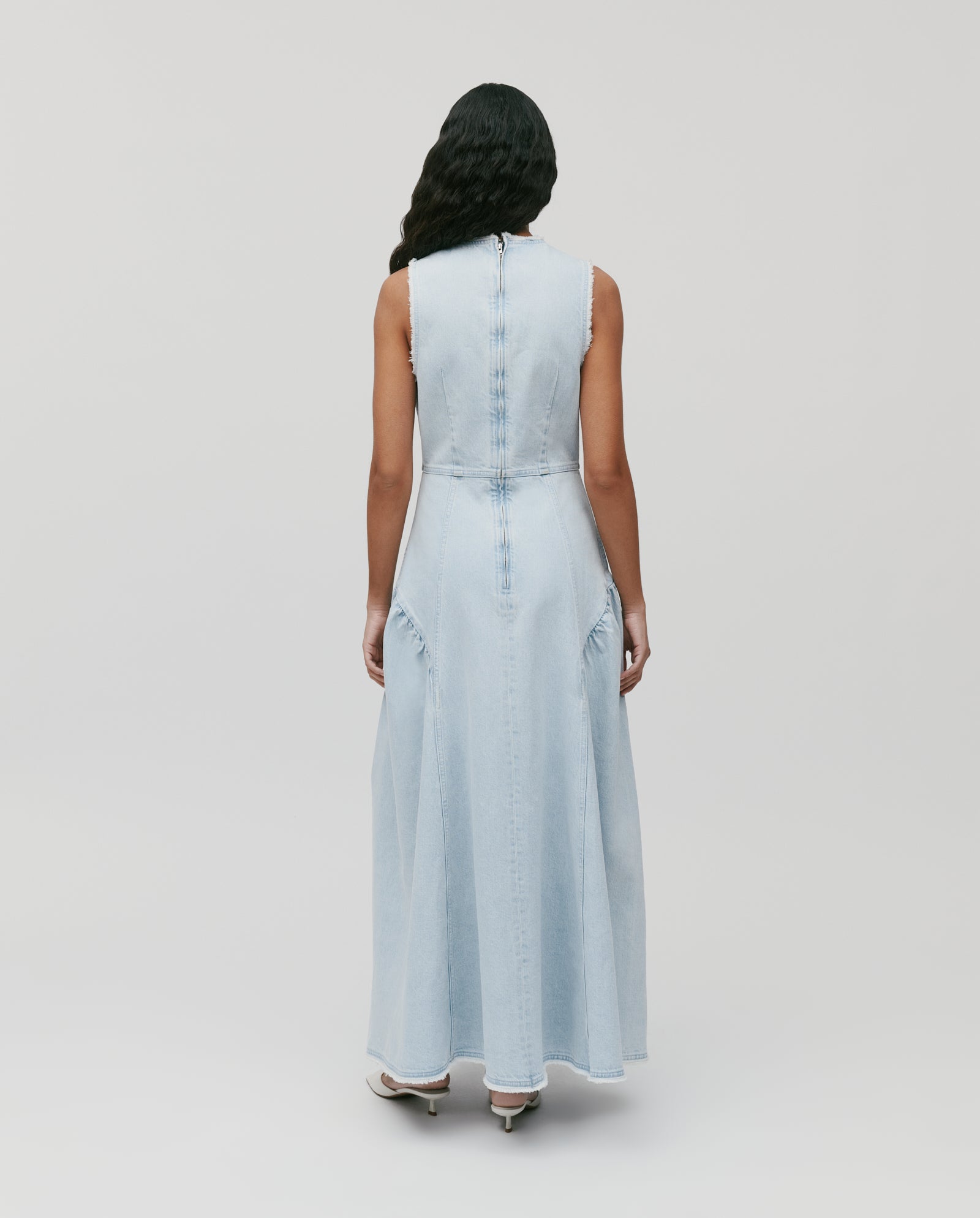 A woman stands facing away against a white background, wearing the IVY OAK MARCA ANN ankle-length sleeveless denim dress with fringe details.