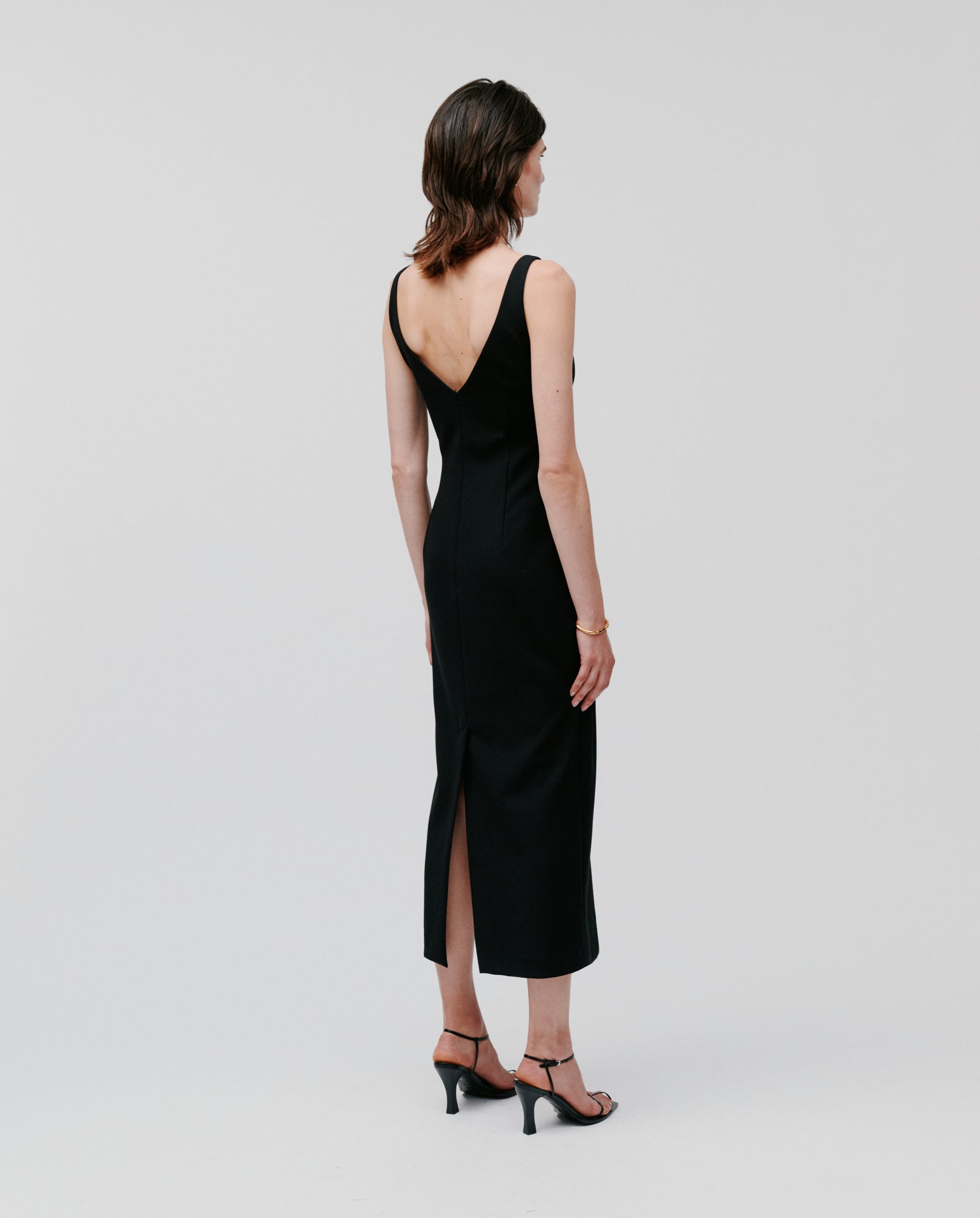 A woman in a sleeveless, ankle-length IVY OAK NEPHELIA Dress made from matte fabric and heels stands with her back to the camera against a plain background.