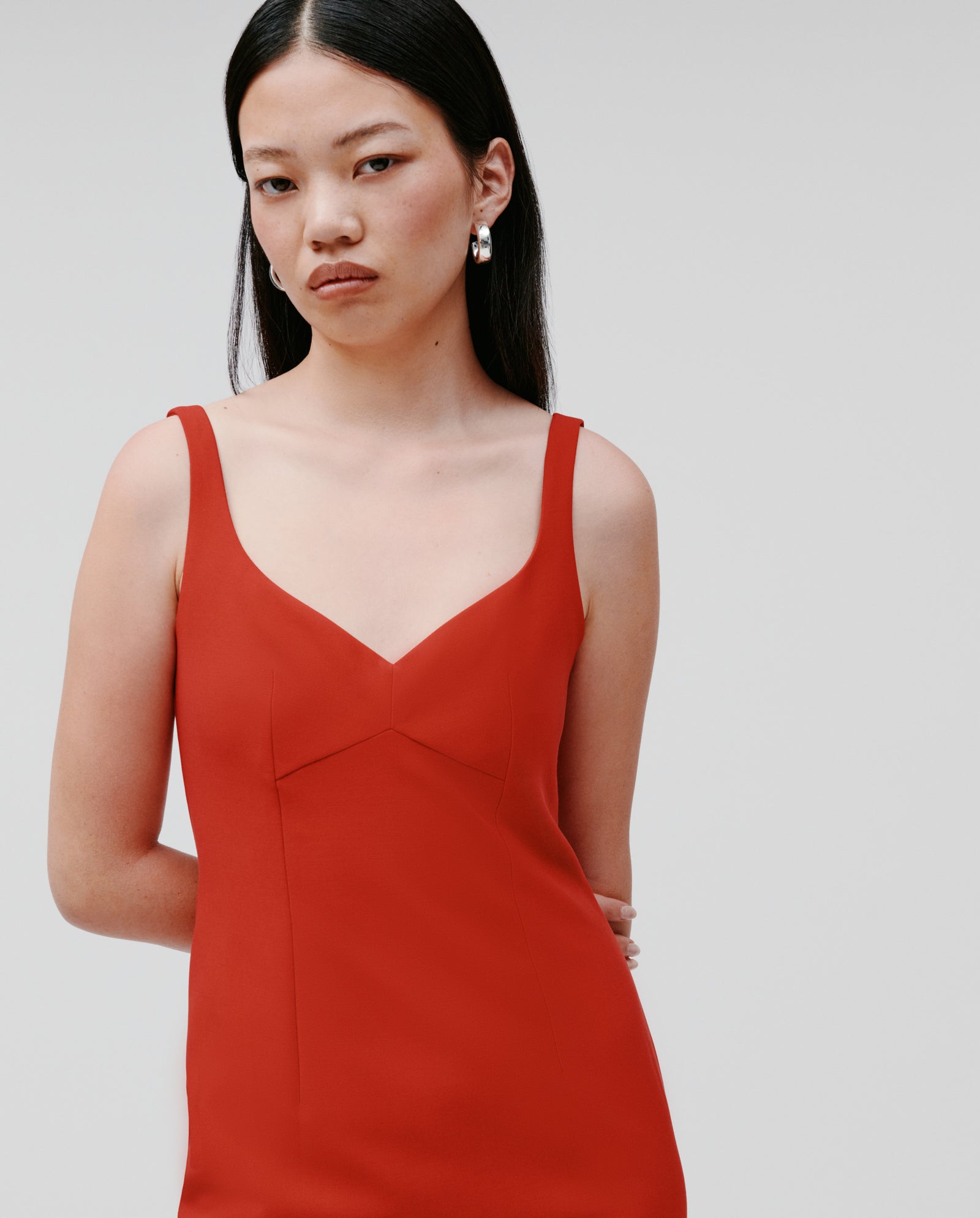 A woman with long dark hair wears the sleeveless, ankle-length NEPHELIA Dress by IVY OAK in matte red with a high slit, looking at the camera with a neutral expression.