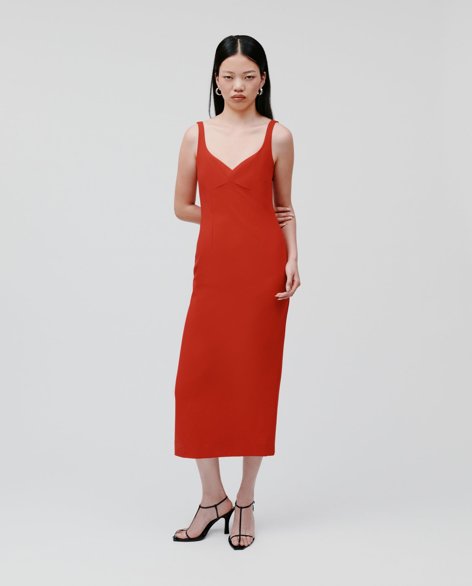 A woman models the IVY OAK NEPHELIA Dress, an ankle-length red gown with a long slit, paired with black heels, against a plain white background.