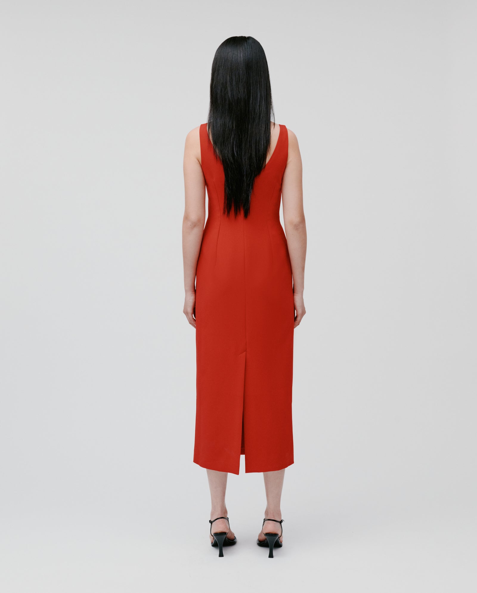 Woman with long dark hair stands facing away, wearing the IVY OAK NEPHELIA sleeveless ankle-length red dress with a long slit and black heels.
