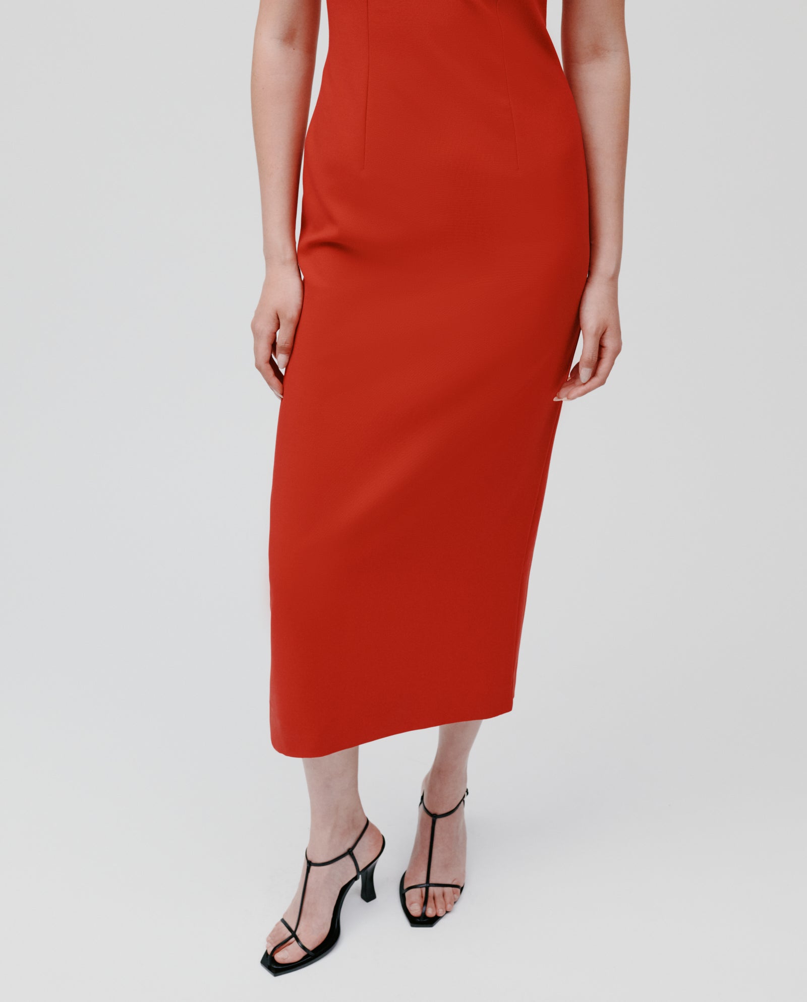 A woman models the NEPHELIA Dress by IVY OAK—an ankle-length, matte-finish dress with a long slit—paired with black heeled sandals against a plain background.