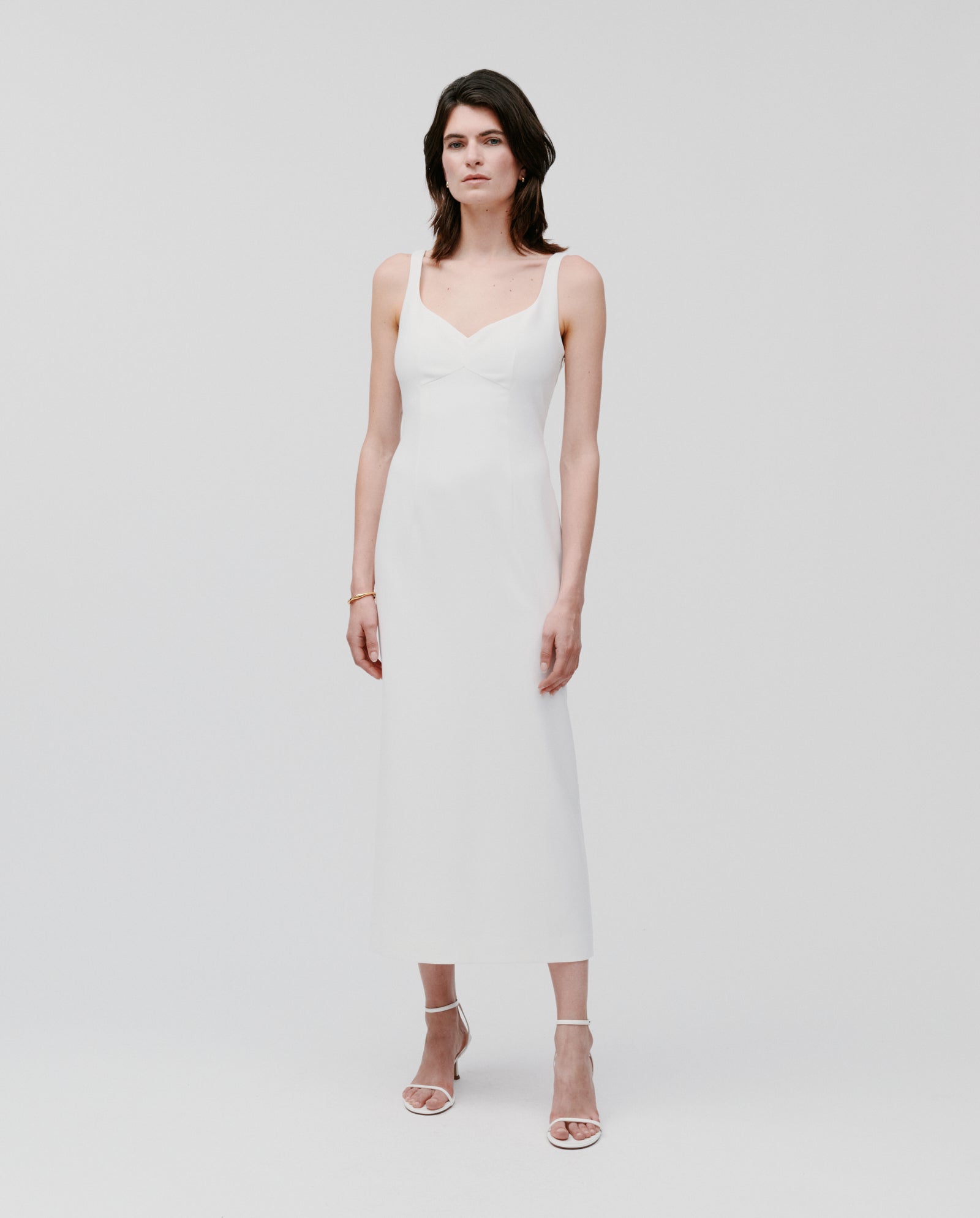 A woman wears the IVY OAK NEPHELIA sleeveless, white ankle-length matte dress with white heels, standing against a plain light background.