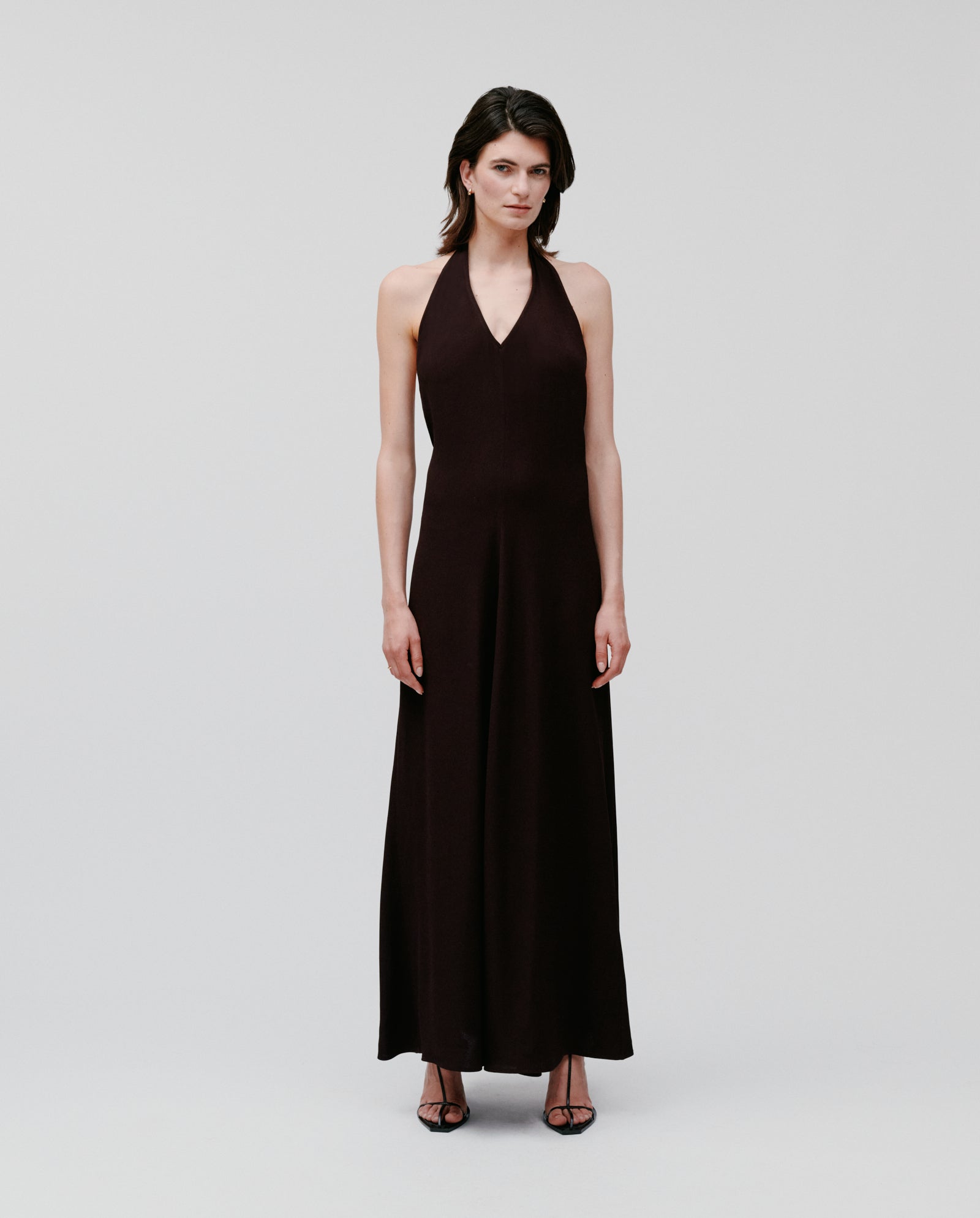 A woman models the IVY OAK NESTA dress, a sleeveless neckholder style in crepe fabric, paired with black heels and photographed against a plain background.