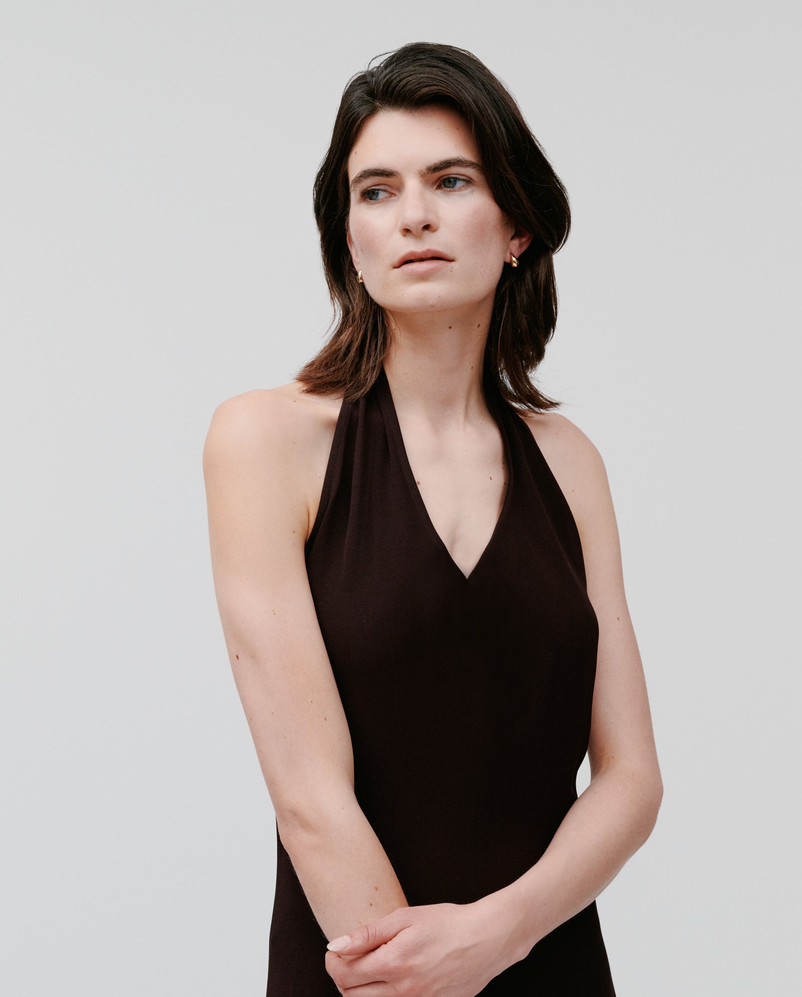 Woman with shoulder-length dark hair wears the IVY OAK NESTA sleeveless black neckholder dress in crepe, set against a plain light background.