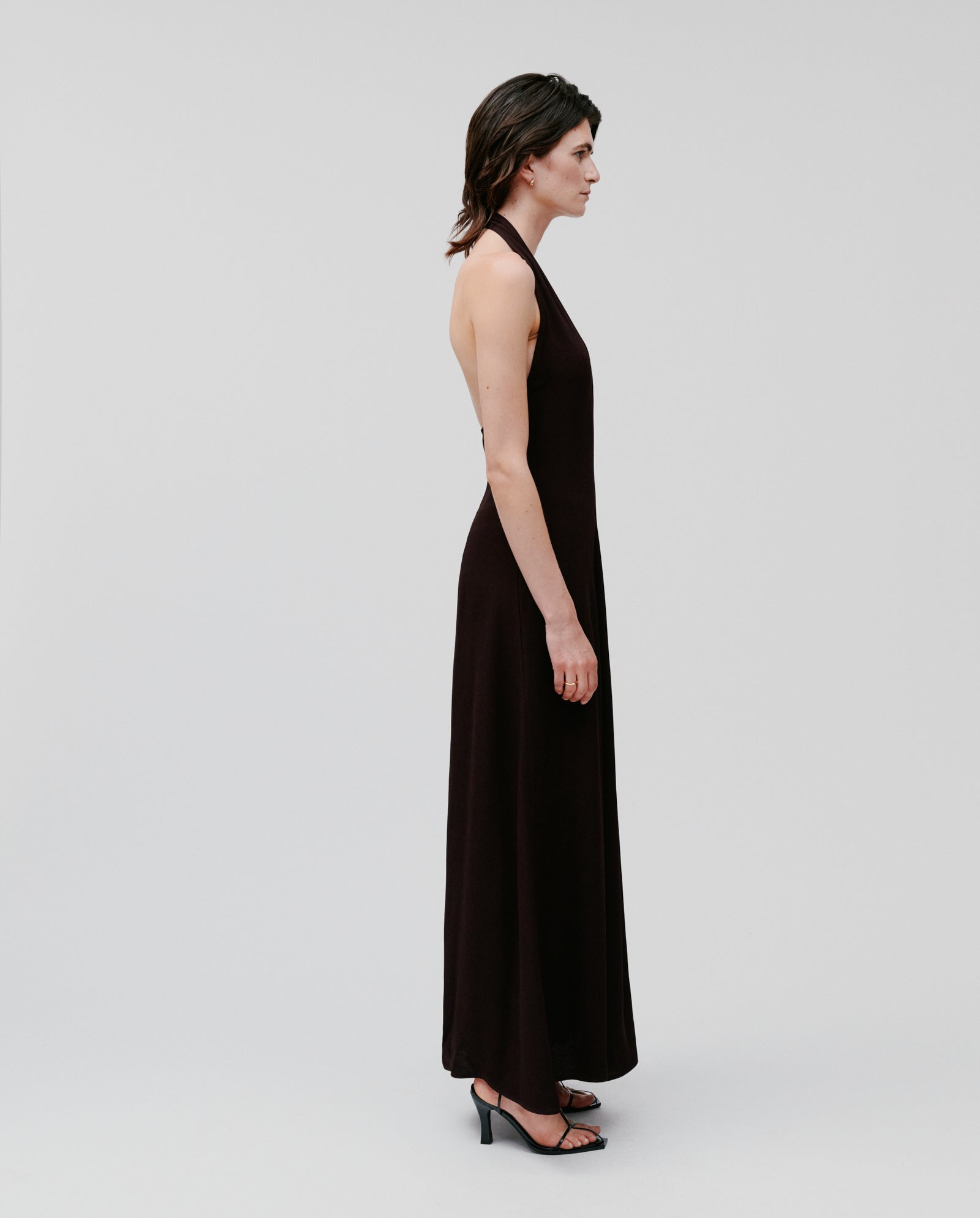 Woman wearing the IVY OAK NESTA sleeveless black crepe neckholder dress with heels, standing in profile against a plain background.