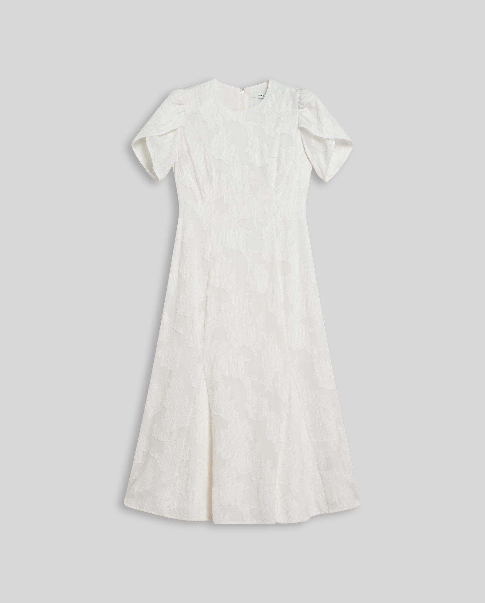 The IVY OAK NASRIN Dress is a white short-sleeve midi with a fitted bodice and subtle fil coupé texture, shown laid flat on a light gray background.