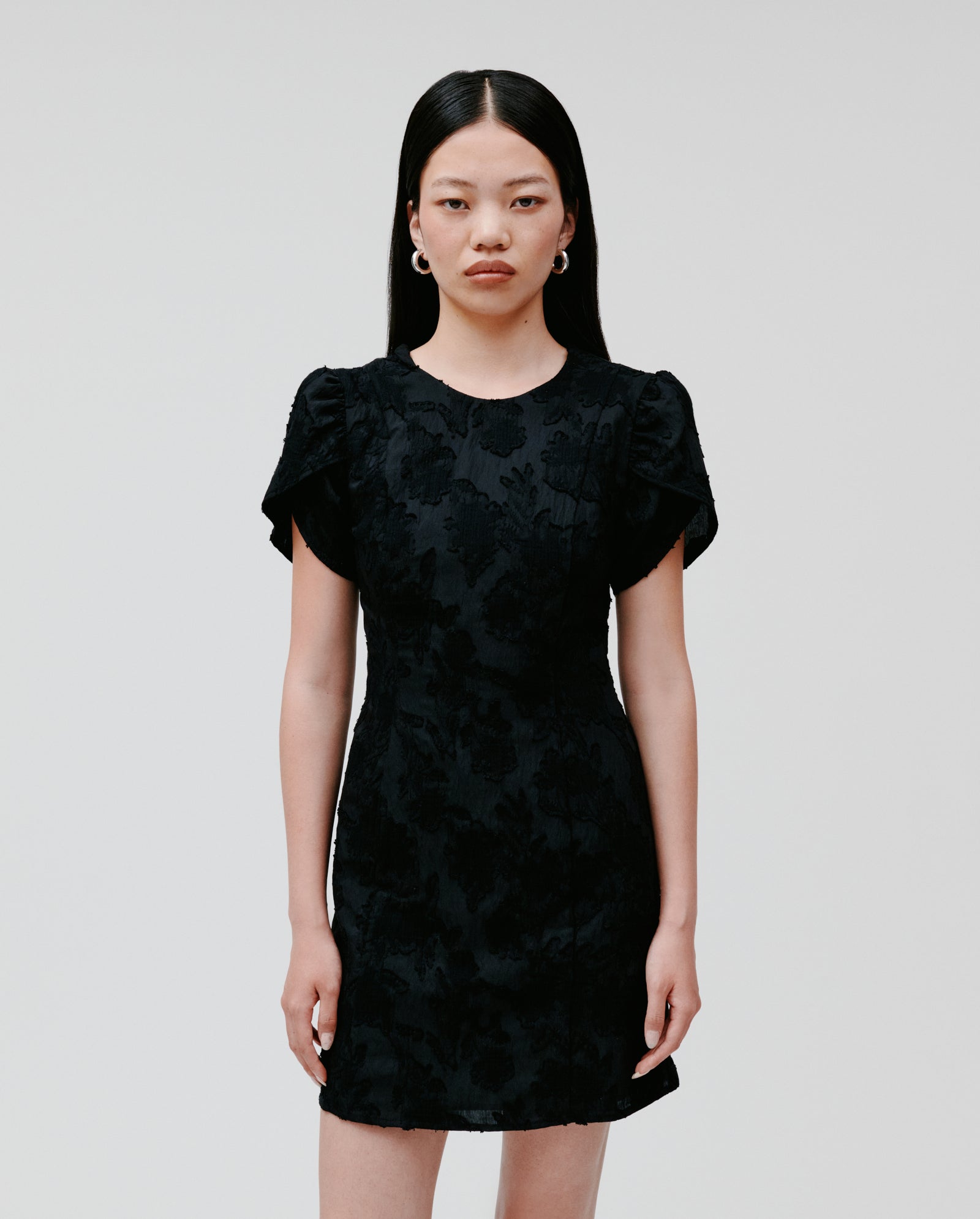 A woman wears the IVY OAK NERISSA Dress, a black fil coupé mini dress with puff sleeves, standing against a plain white background.