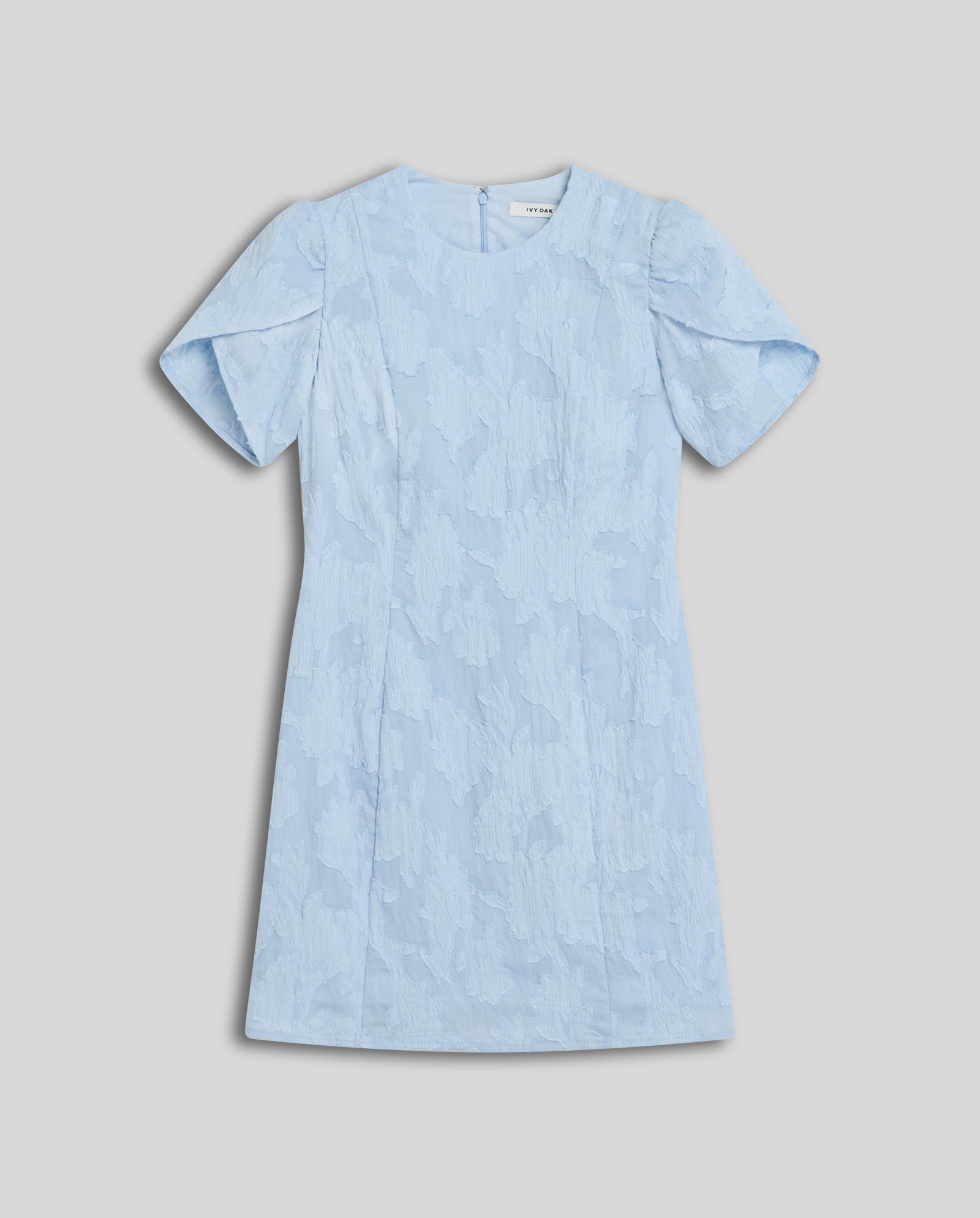 The IVY OAK NERISSA Dress is a light blue fil coupé mini dress with a textured floral pattern, short sleeves, and an elegant A-line silhouette, shown laid flat on a light gray background.