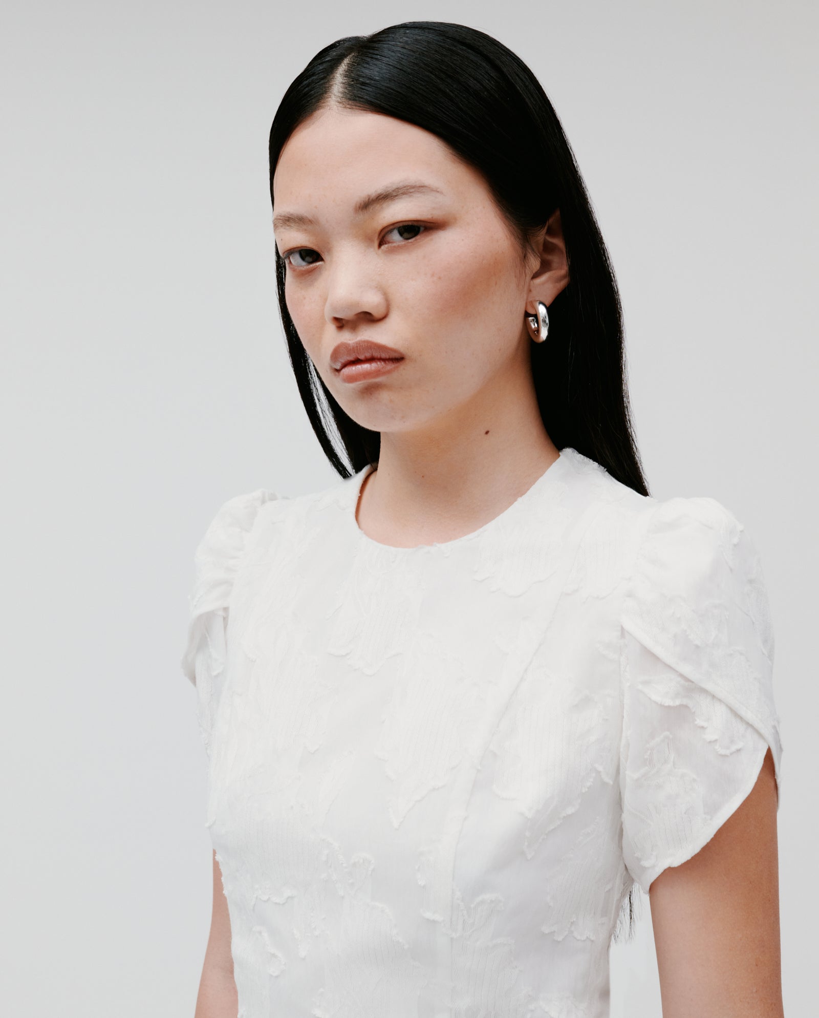 Woman with long black hair wears the IVY OAK NERISSA Dress, a textured fil coupé mini dress, paired with silver hoop earrings as she looks at the camera.