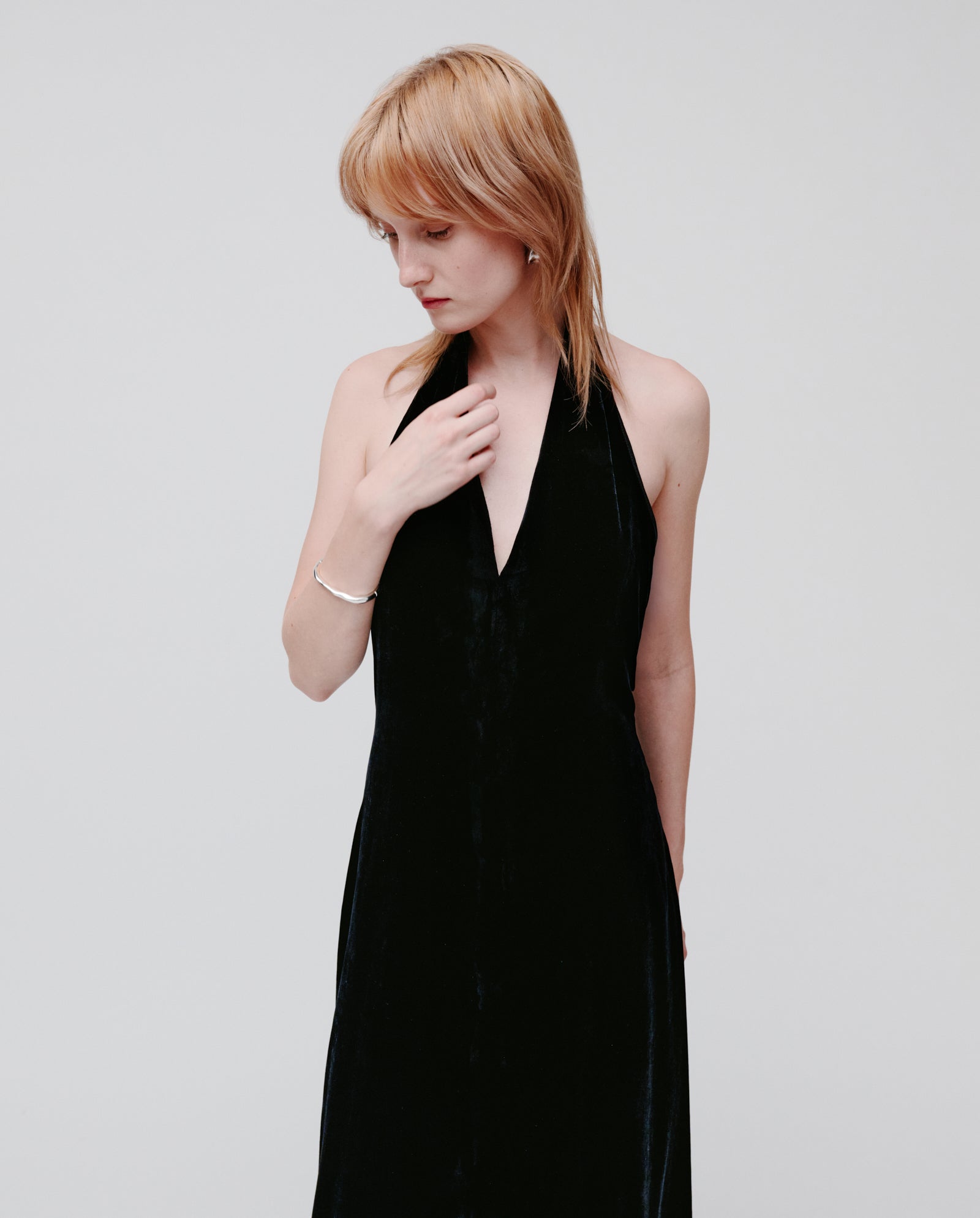 A person wearing the IVY OAK NESTA ROSE sleeveless black neckholder dress looks down, touching their collar with one hand against a plain background.