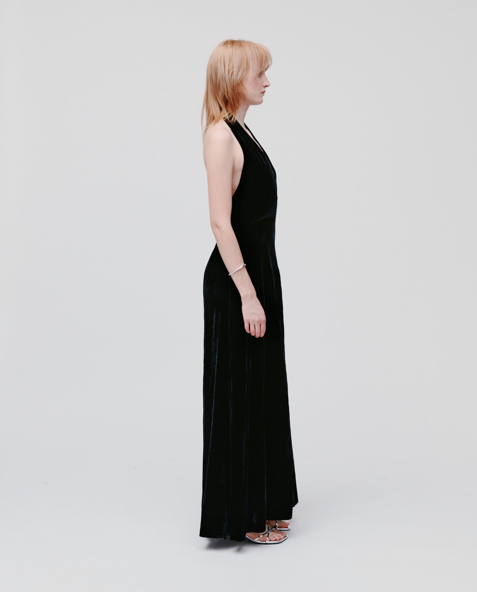A woman in profile wears the IVY OAK NESTA ROSE Dress, a black velvet midi with a zipper closure, against a plain light background.