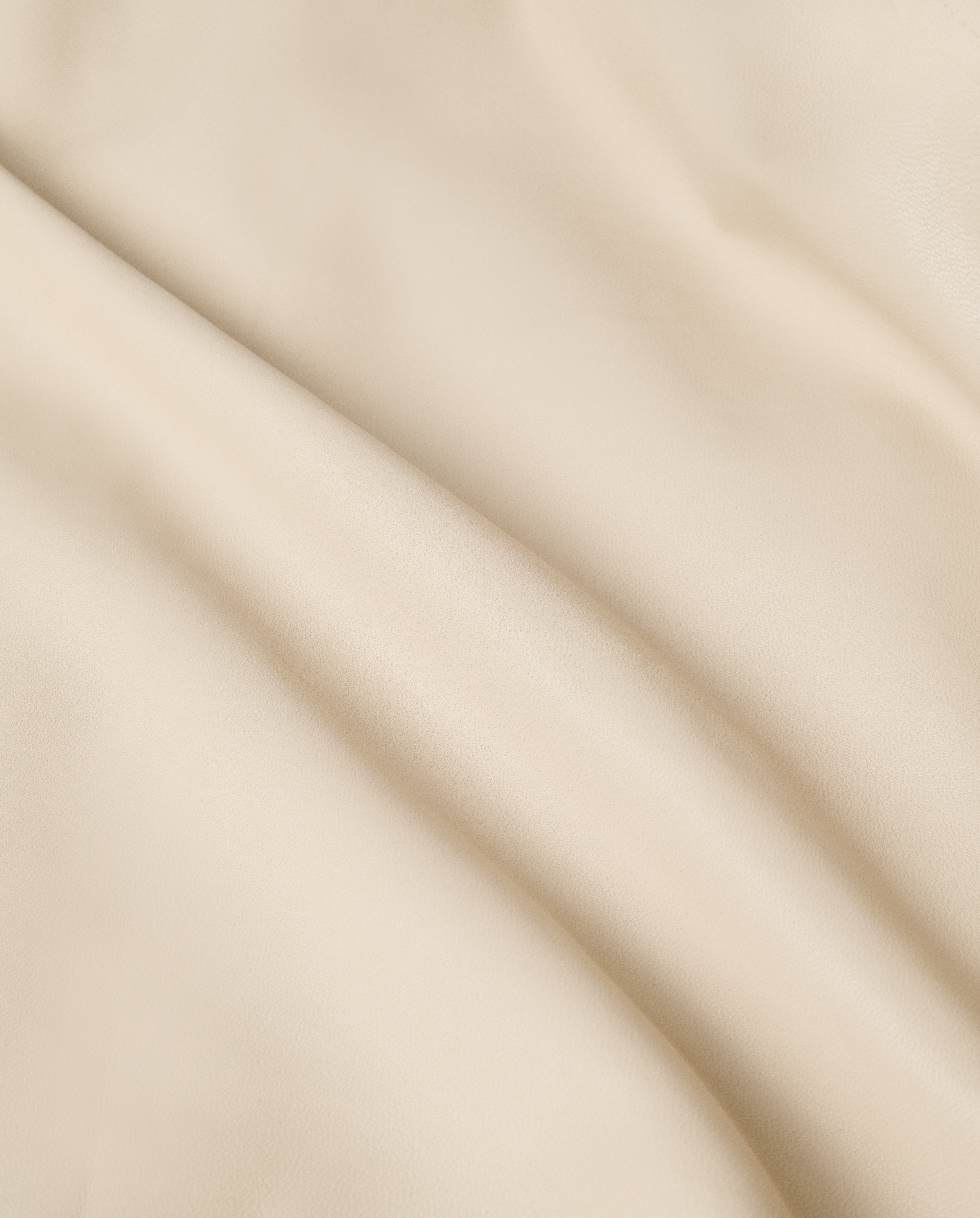 Close-up of the LILITH Coat by IVY OAK, showcasing smooth beige fabric with gentle folds and a soft, slightly textured surface, reminiscent of a classic trench coat.
