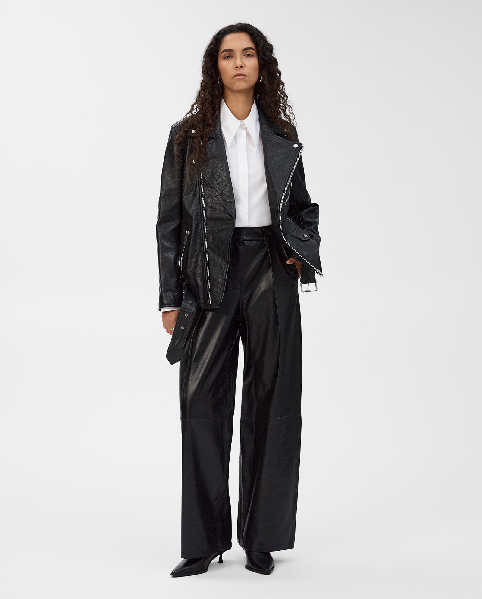 A woman stands confidently in the IVY OAK LENNY Jacket, styled with wide-leg leather pants, a white shirt, and black heels for a cool boyfriend look.