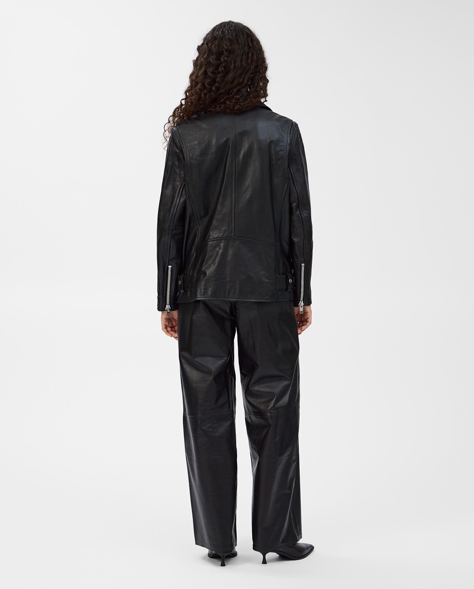 Person with long curly hair wears the oversized LENNY Jacket by IVY OAK and pants, standing with their back to the camera for a cool, relaxed look.