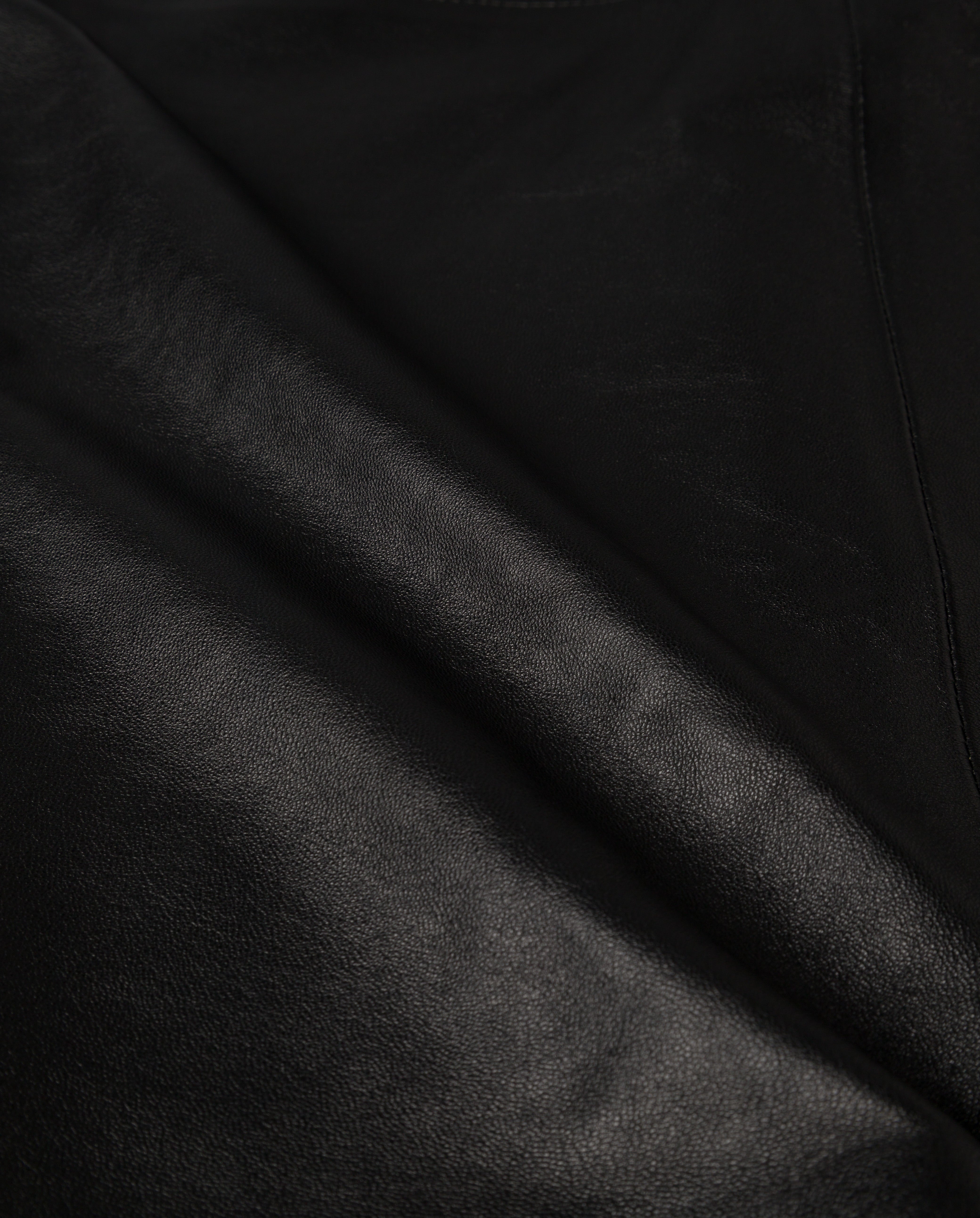 Close-up of smooth, shiny black leather with subtle texture and light reflections, ideal for the LEXIE Skirt by IVY OAK.