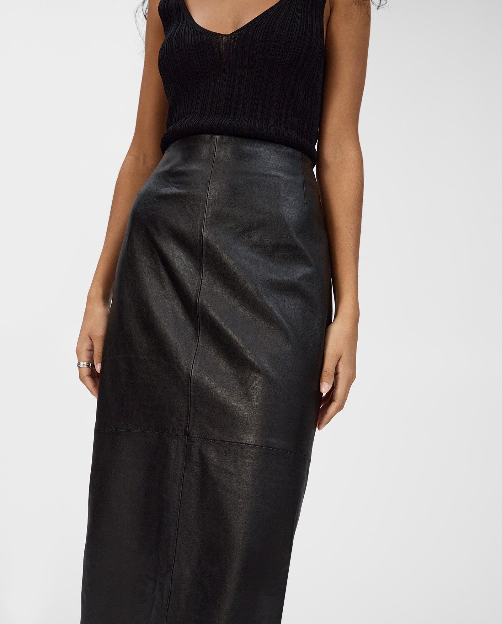 Model wears the IVY OAK LEXIE Skirt, a high-waisted, midi-length black leather style, paired with a sleeveless black top against a plain background.