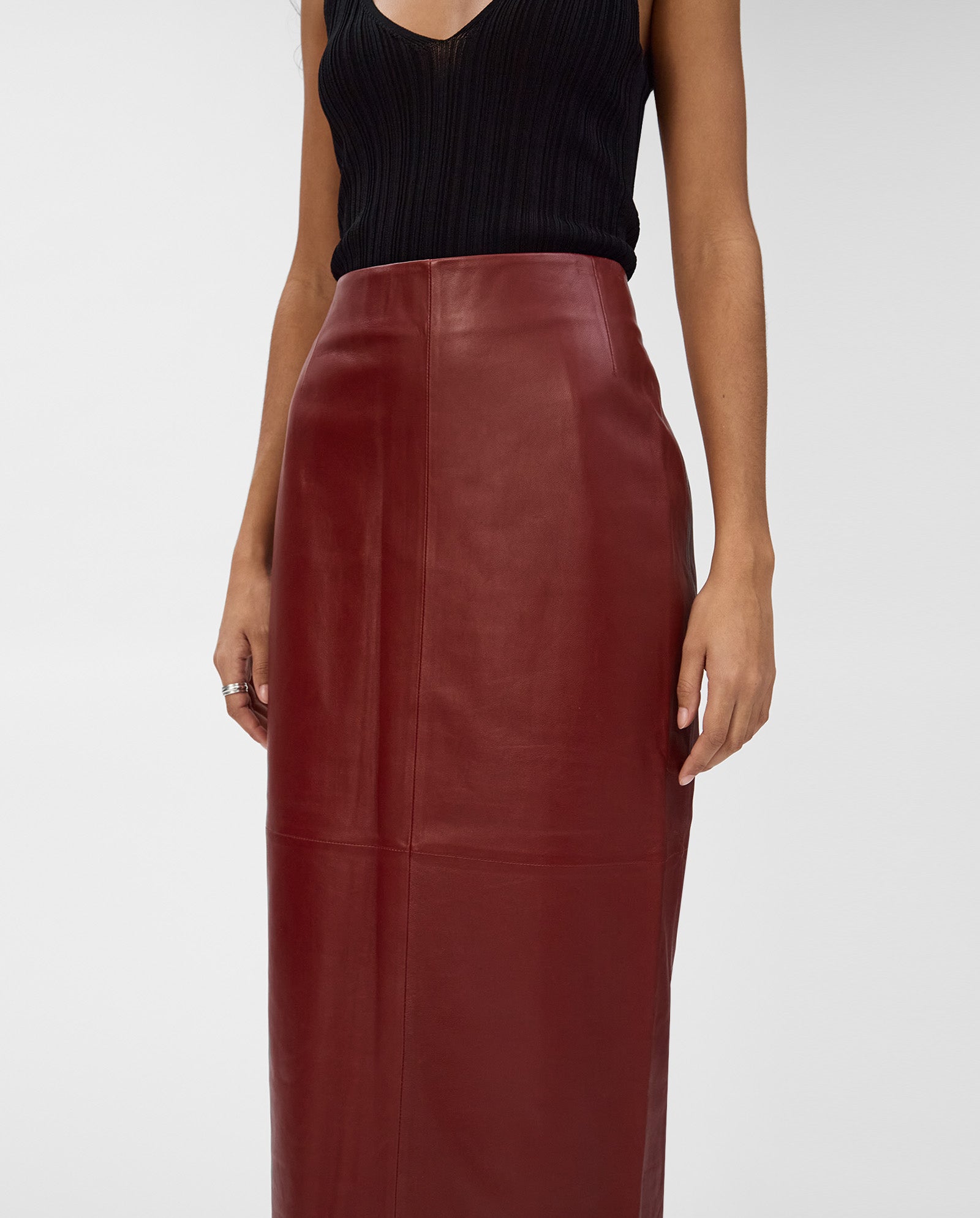 Woman wearing a sleeveless black top and the IVY OAK LEXIE Skirt—a high-waisted, midi-length burgundy leather skirt.