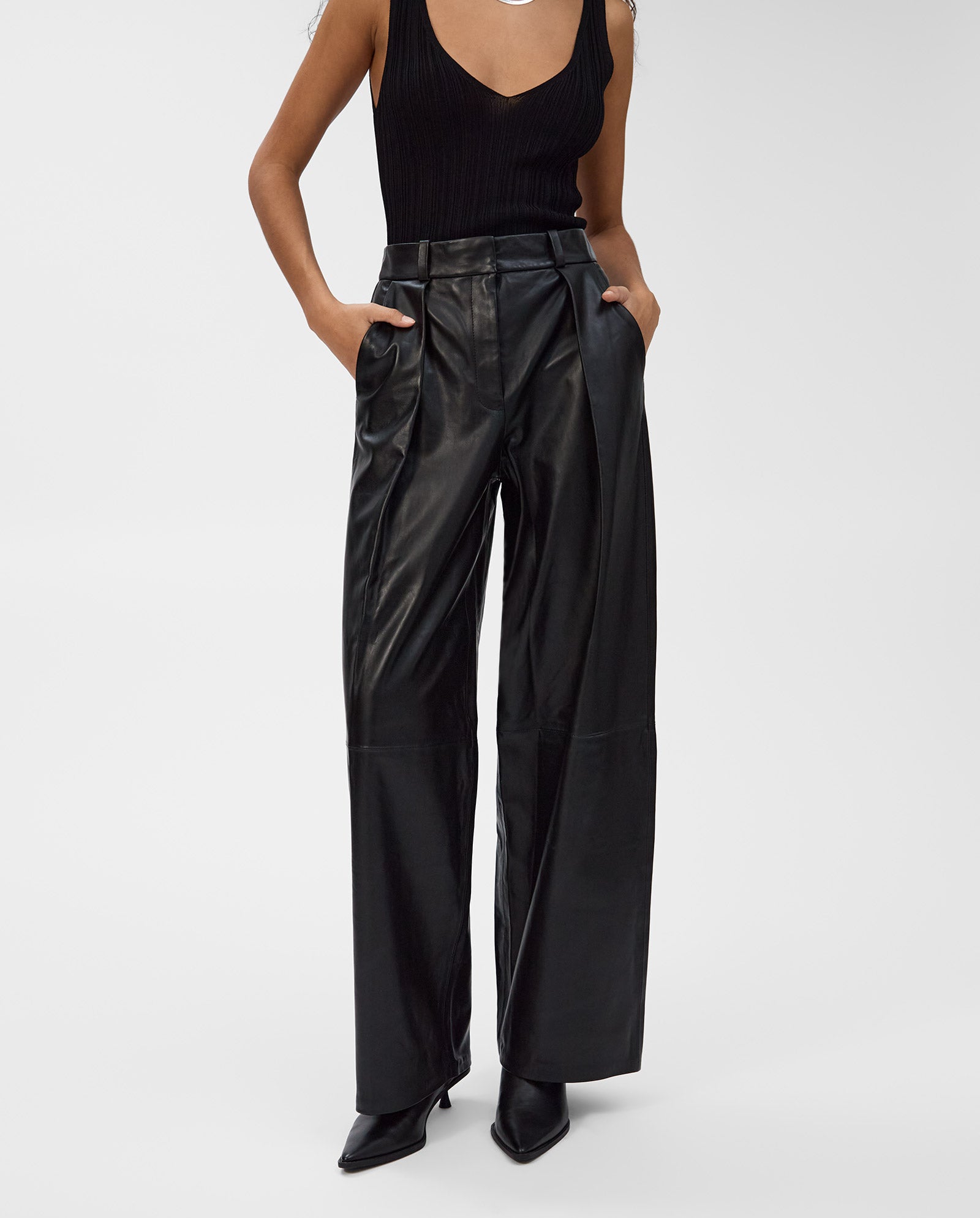 A woman models the IVY OAK LORAINE Trouser—high-waisted, wide-leg leather pants—paired with a sleeveless black top and hands in pockets for a modern look.